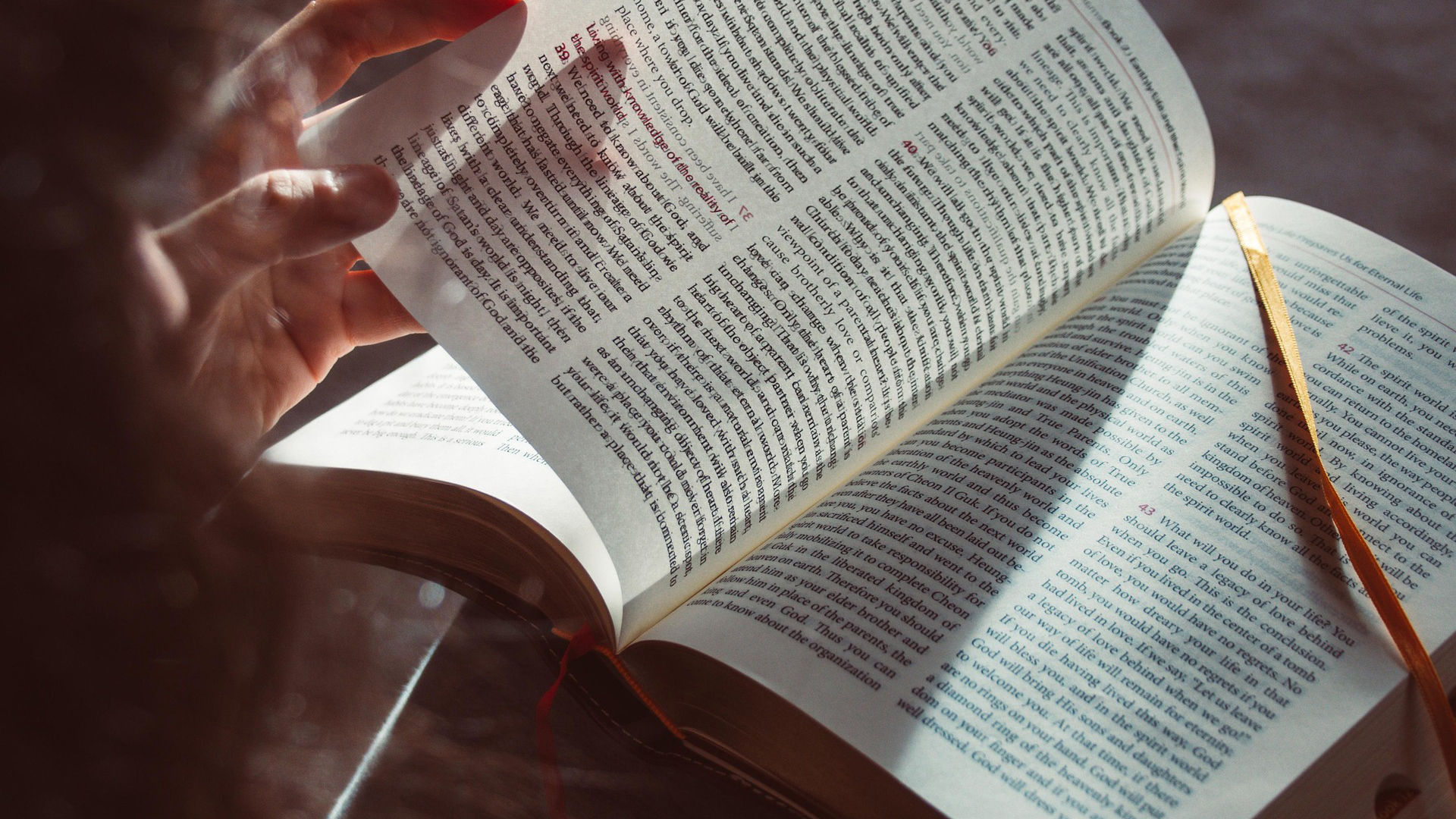 Hand die een bladzijde omslaat in een open boek, met zonlicht en lensflare op de tekst