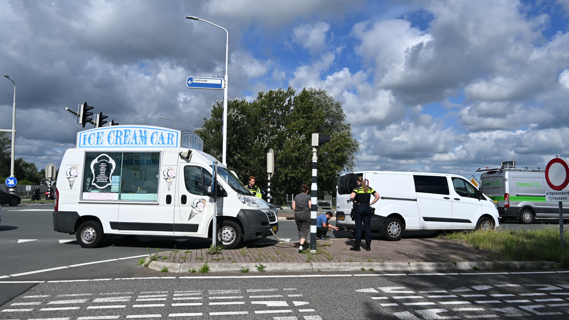 IJswagen met bord Ice Cream Car staat stil bij kruispunt, naast een witte bestelbus en politie op de weg