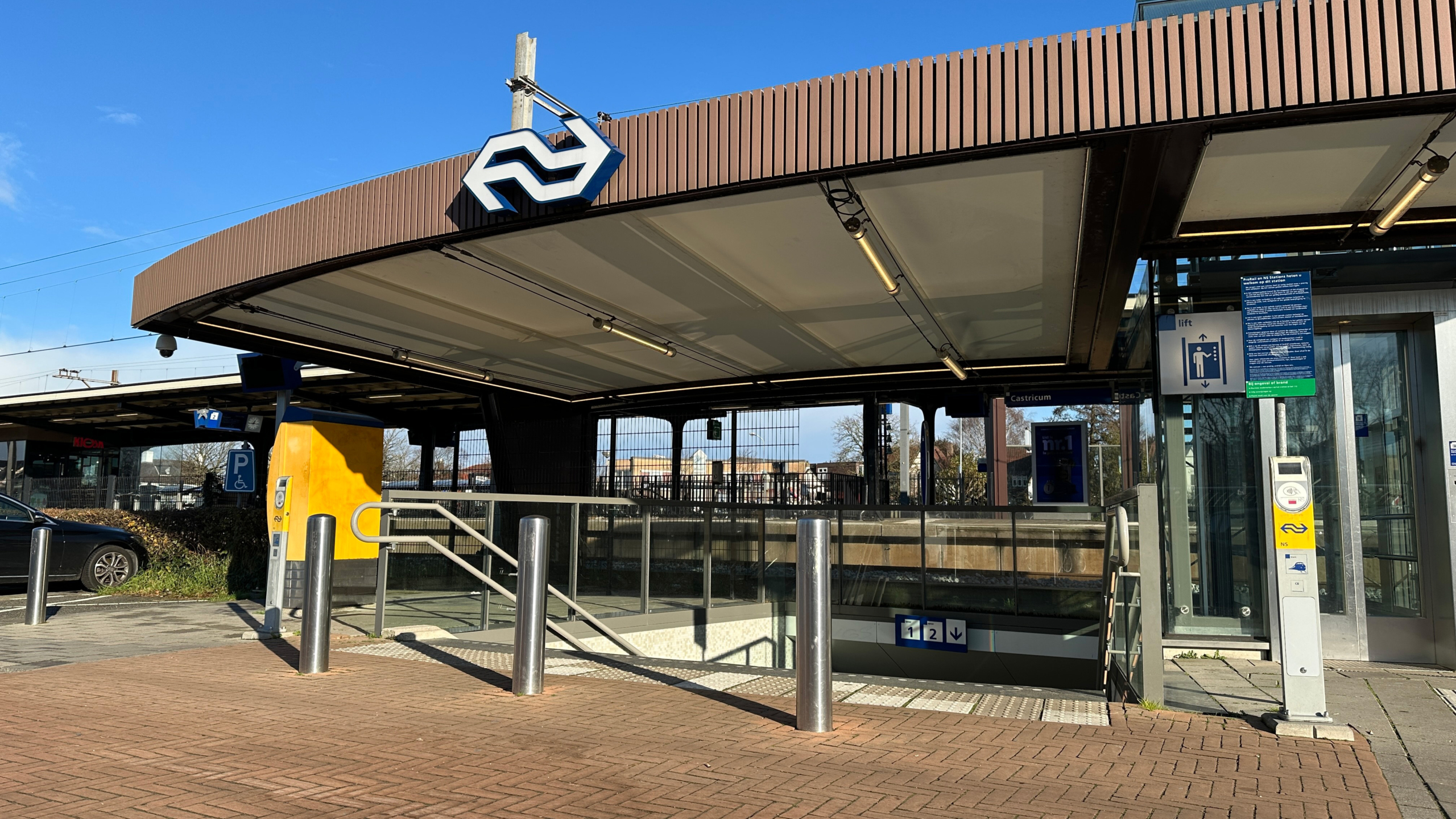 Ingang van treinstation Castricum met NS-logo, liftbord en trap naar perrons 1 en 2 onder een overkapping