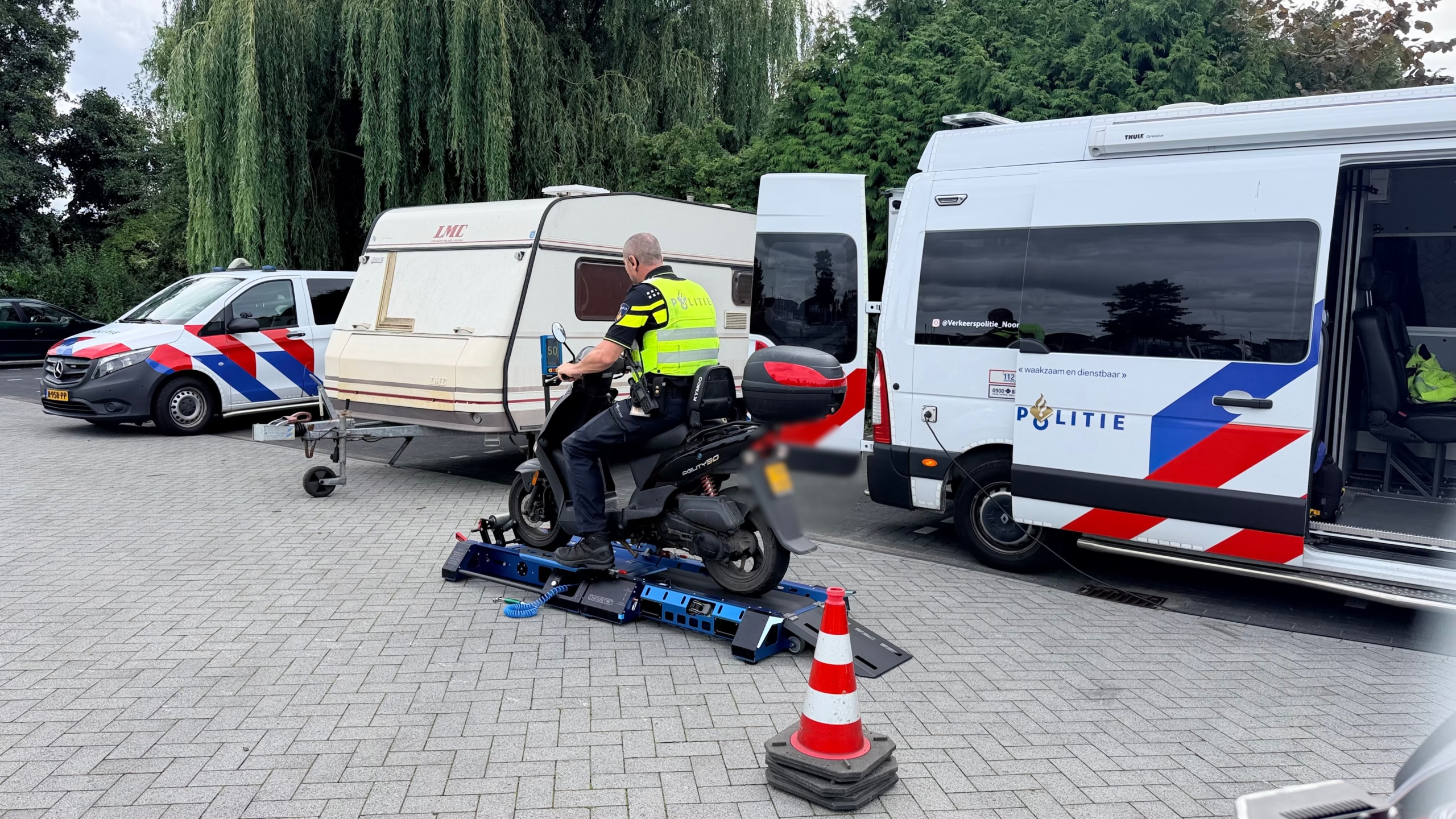 Politieagent op een scooter op een testbank, met politievoertuigen en een caravan op de achtergrond