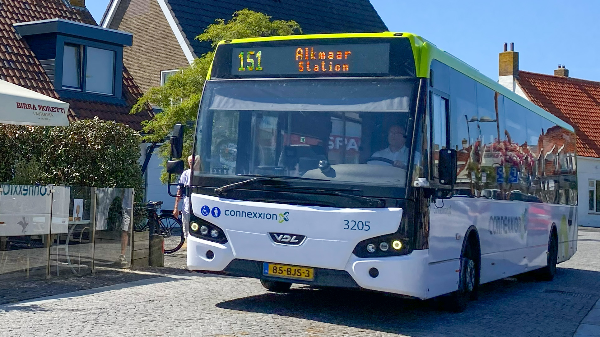 Connexxion-bus lijn 151 richting Alkmaar Station rijdt door een dorp met huizen op de achtergrond