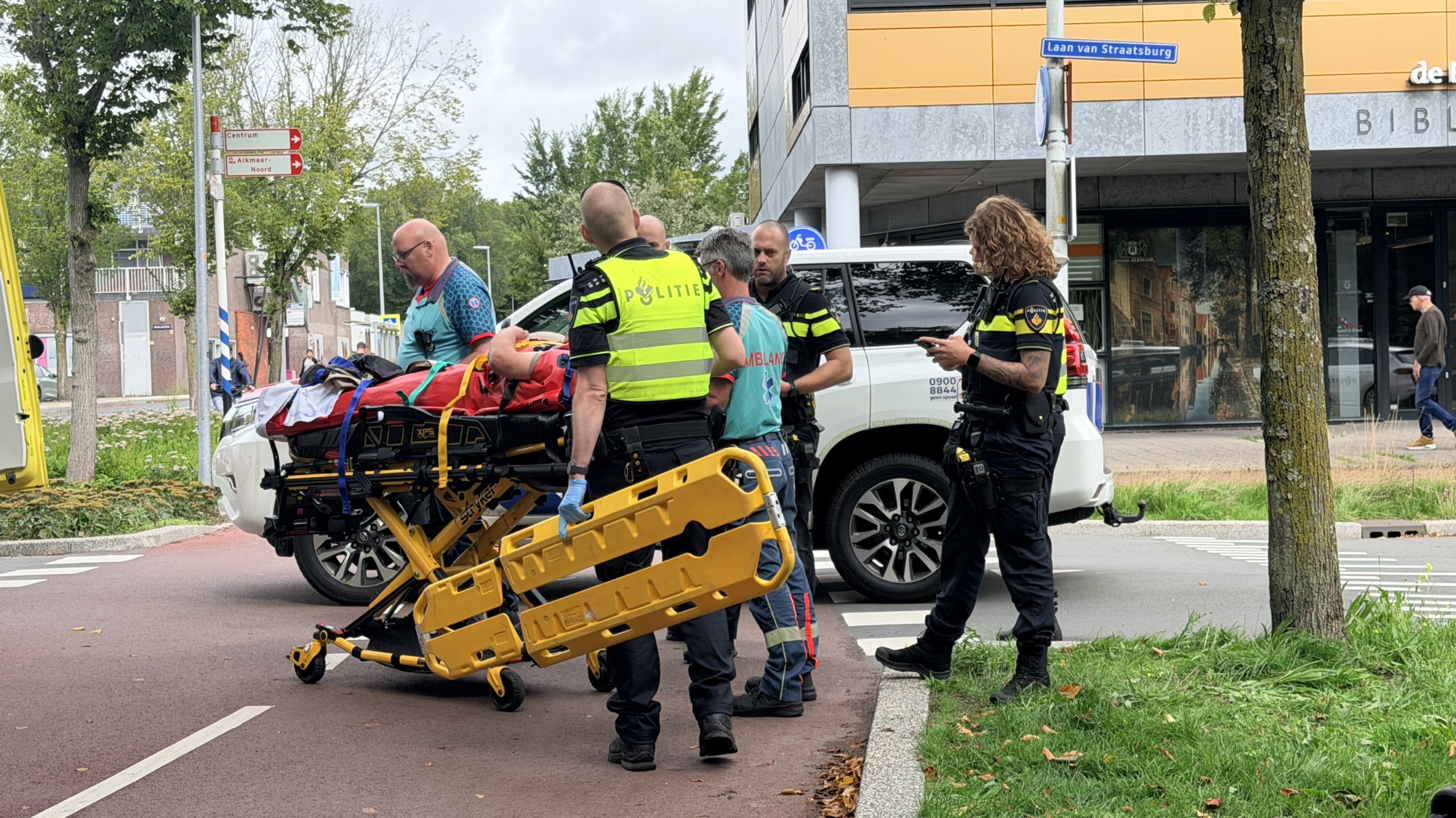 Politie en ambulancepersoneel met brancard en geel wervelplank bij een wit politiebusje op straat