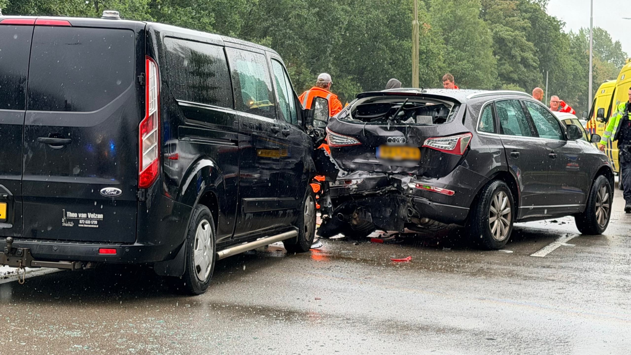 Botsing op natte weg tussen zwarte bestelbus en Audi, met zichtbare schade en hulpdiensten op de achtergrond