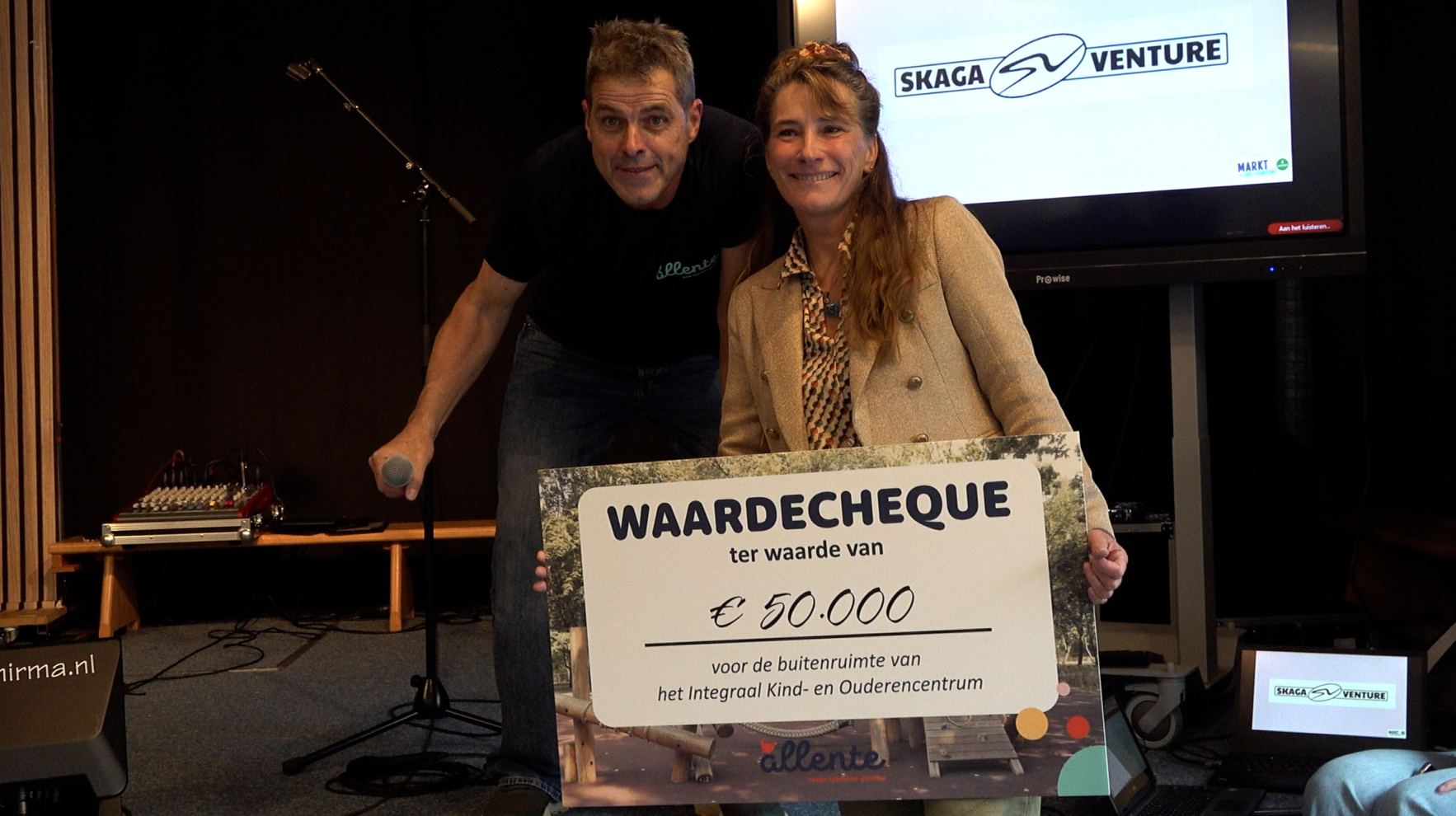 Man en vrouw poseren met een cheque van €50.000 tijdens presentatie; op scherm staat Skaga Venture
