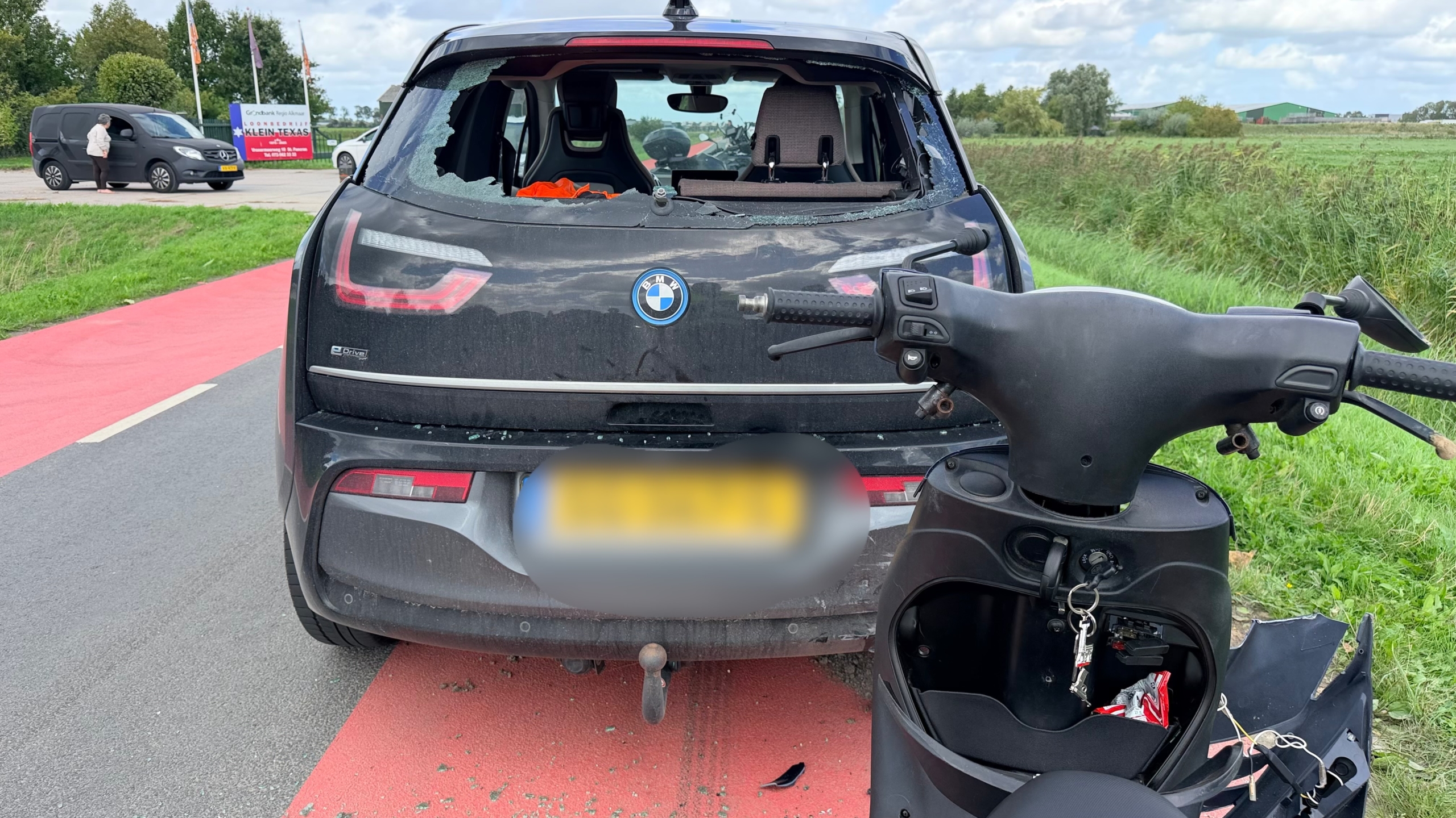 Achterkant van een BMW met ingeslagen achterruit en een beschadigde scooter op de voorgrond langs de weg