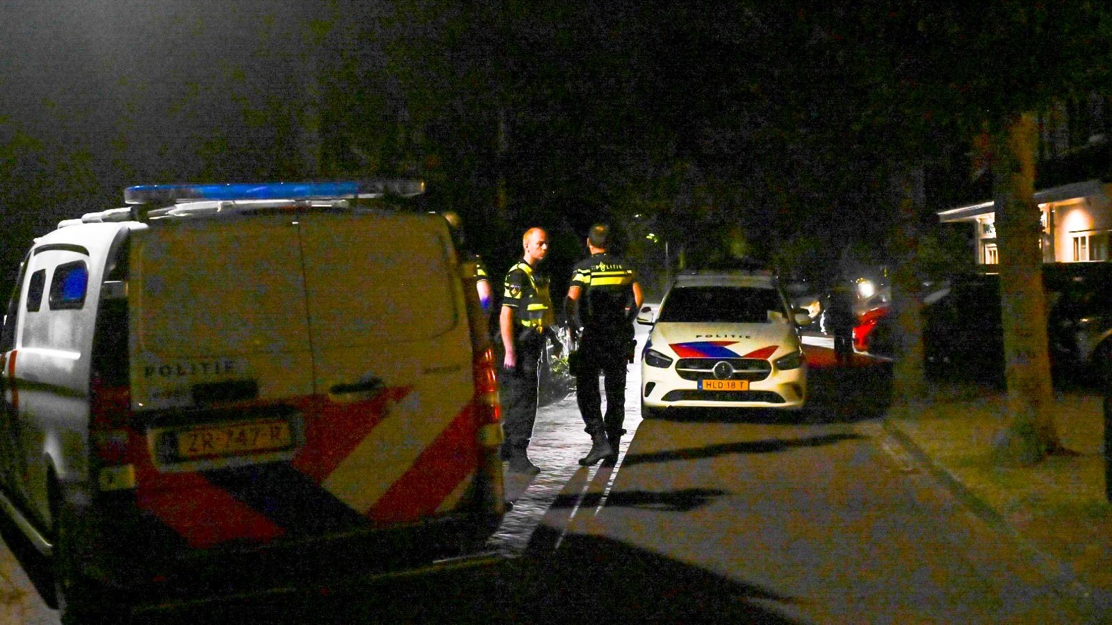 Twee agenten staan ’s nachts op straat tussen politievoertuigen met zwaailichten