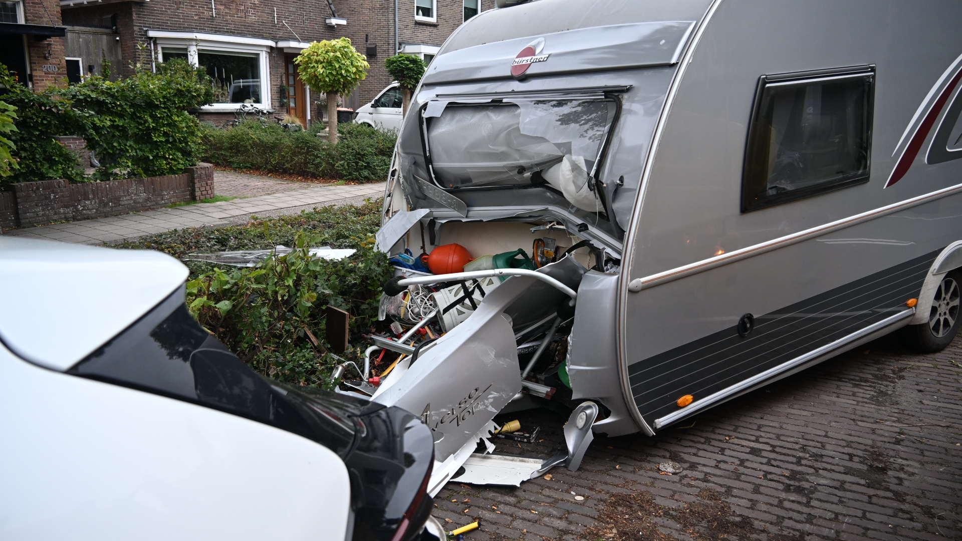Zwaar beschadigde caravan met ingedeukte voorkant na aanrijding, met een auto op de voorgrond in een woonstraat