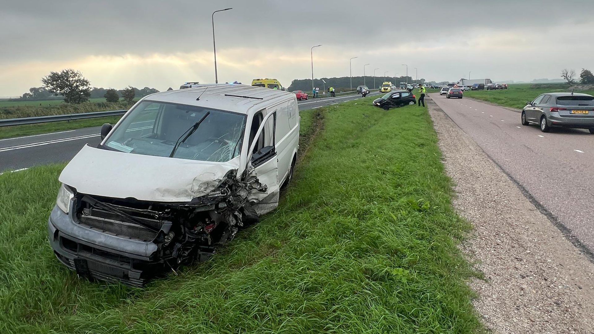 Beschadigde witte bestelbus in de berm naast de snelweg, met hulpdiensten en andere auto’s verderop