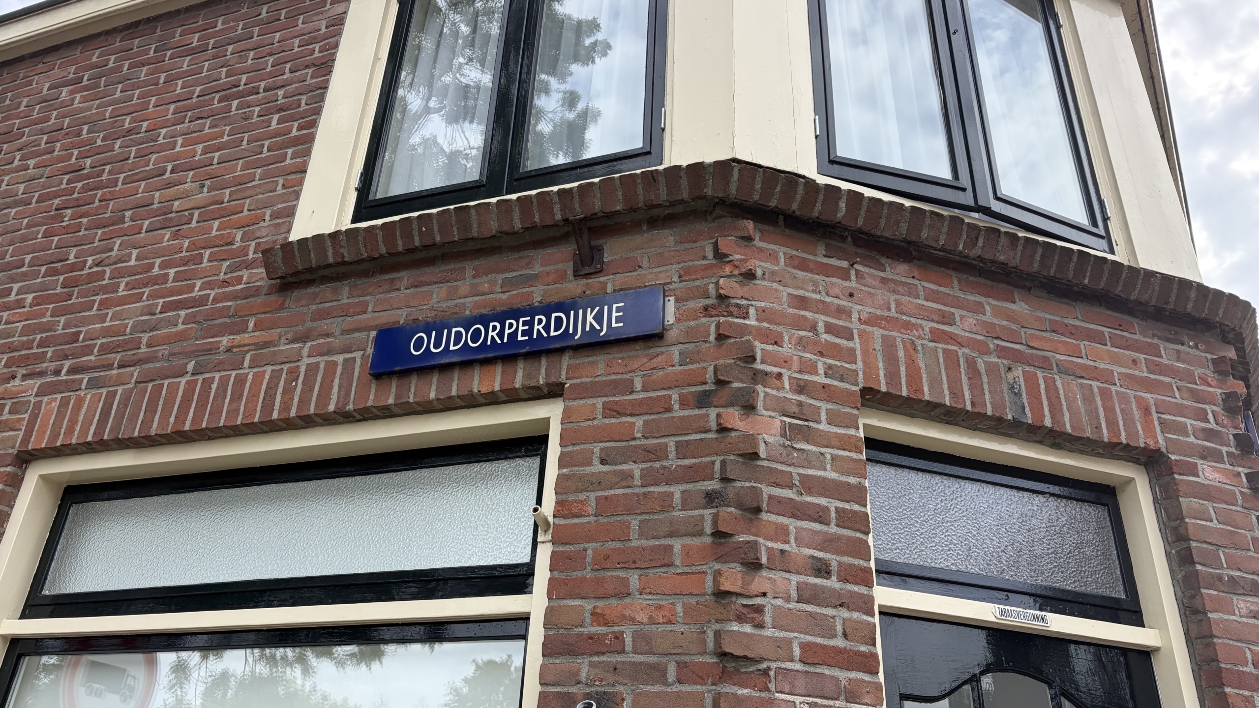 Straatnaambordje met tekst OUDORPERDIJKJE op een bakstenen gevelhoek met ramen erboven