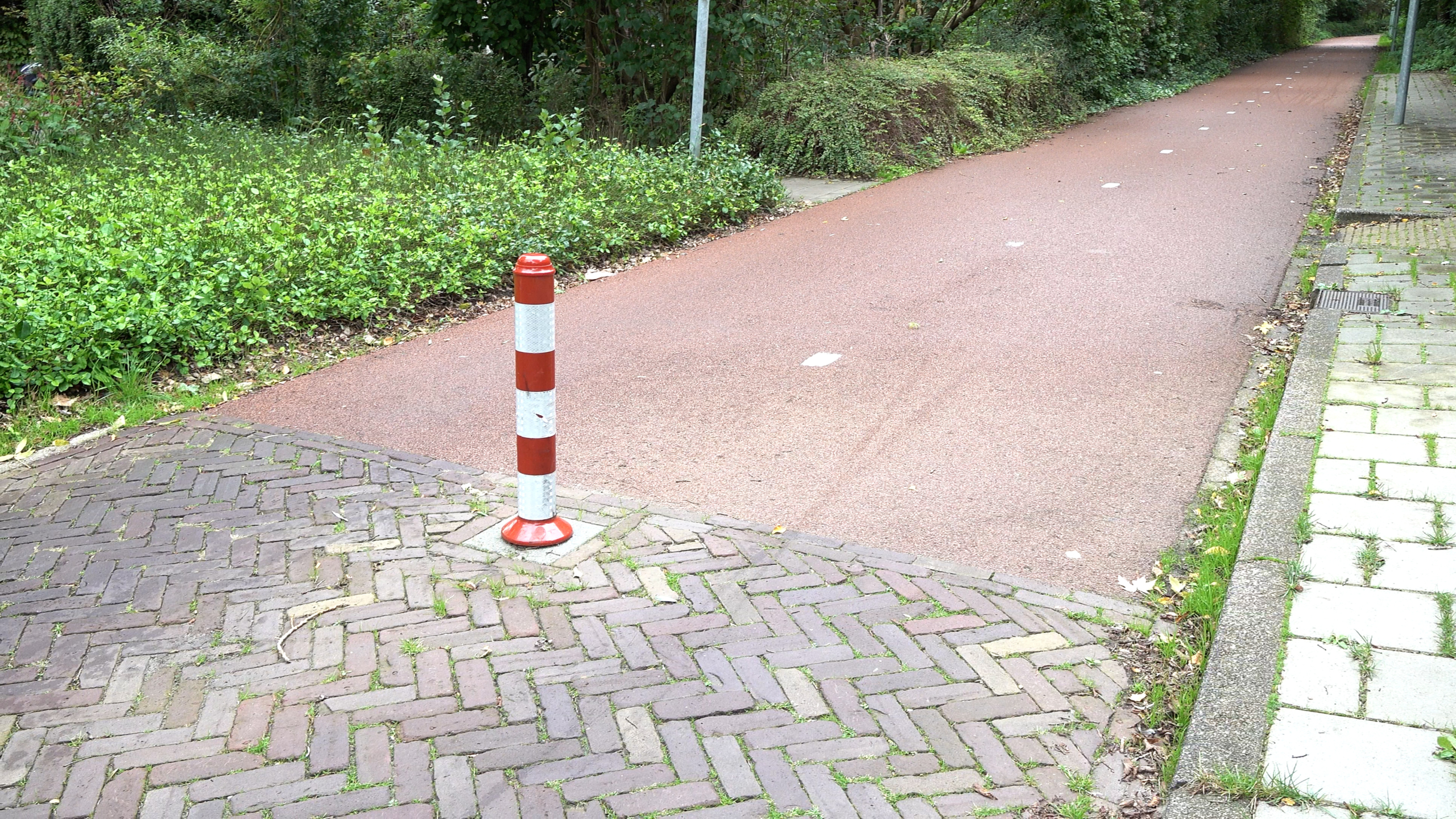 Rood-witte paal naast een rood asfalt fietspad dat langs groen struikgewas en bomen loopt