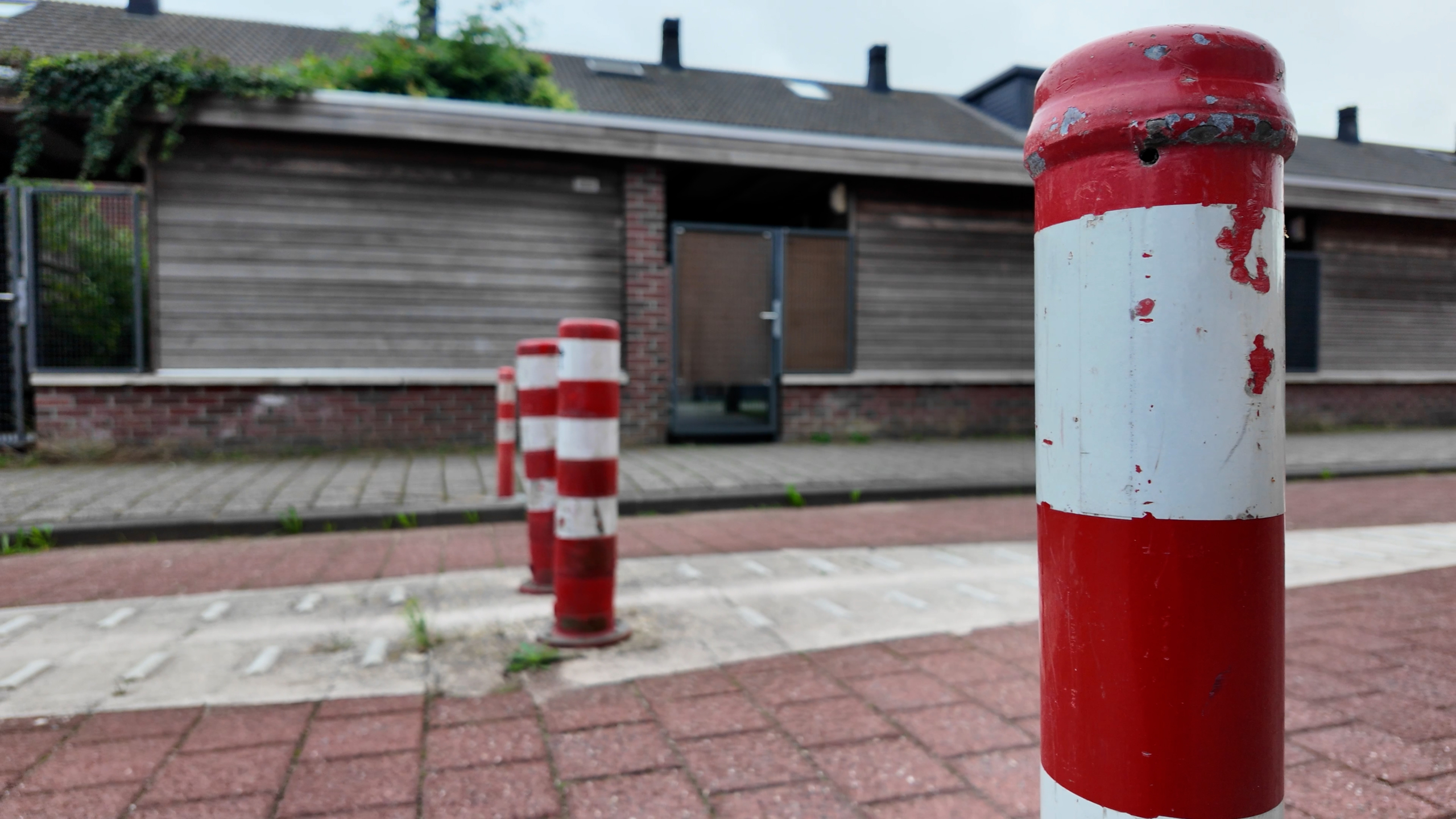 Rood-witte verkeerspaaltjes op een stoep, met een woonhuis en schutting onscherp op de achtergrond
