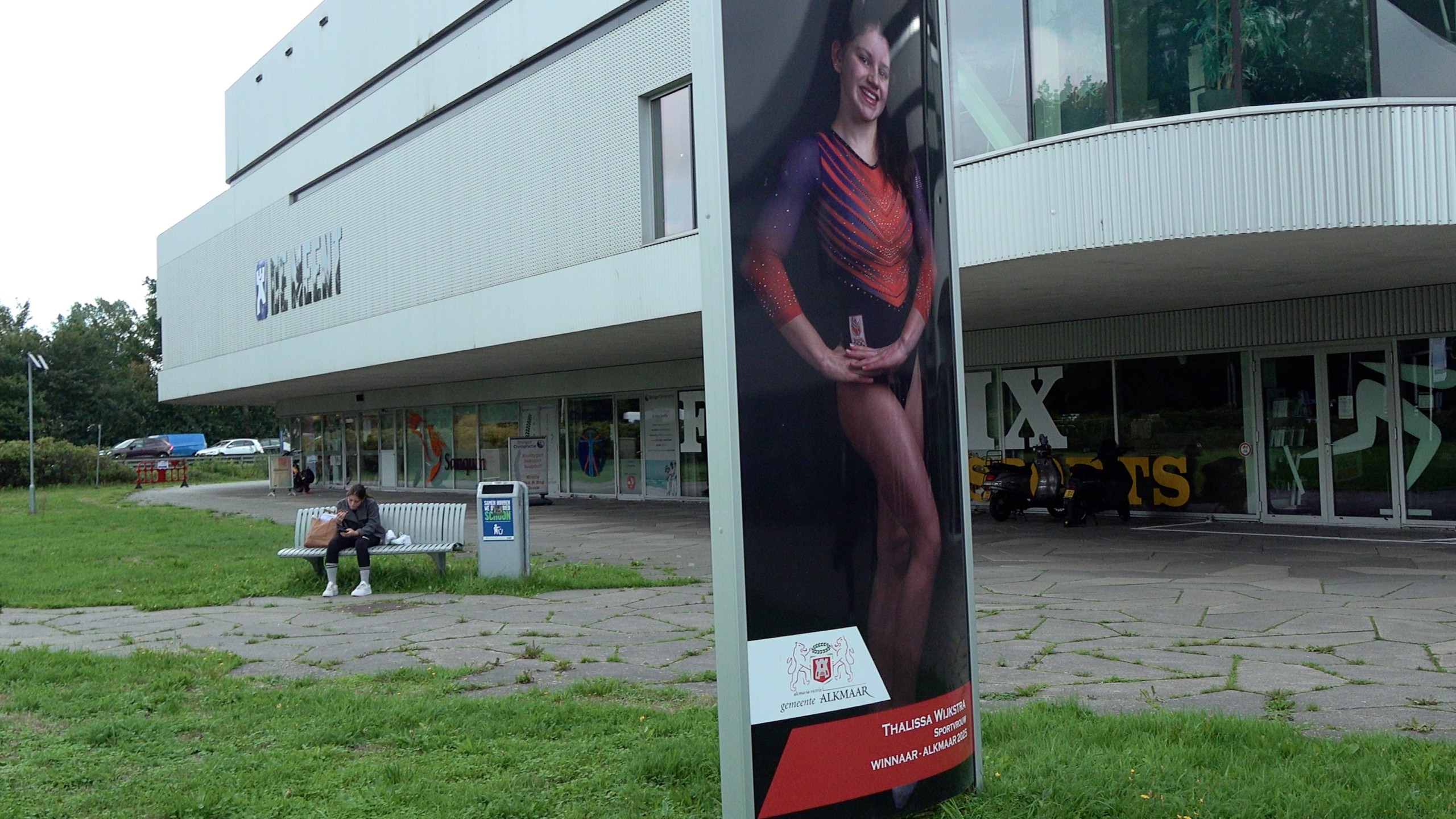 Reclamezuil met foto van een turnster voor een sportgebouw, met op de poster het logo van gemeente Alkmaar