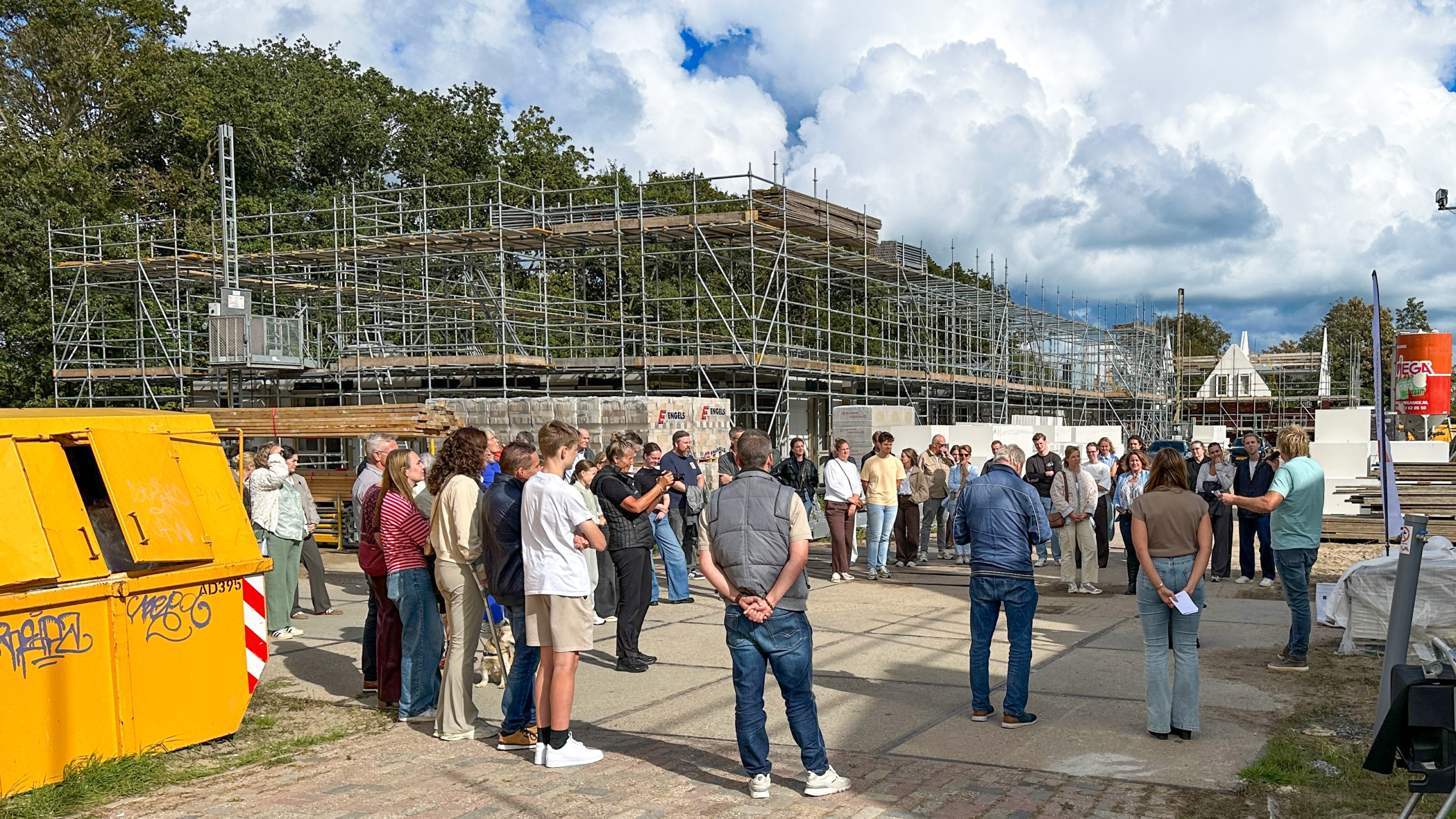 Groep mensen luistert naar uitleg op een bouwplaats met steigers rond een gebouw in aanbouw