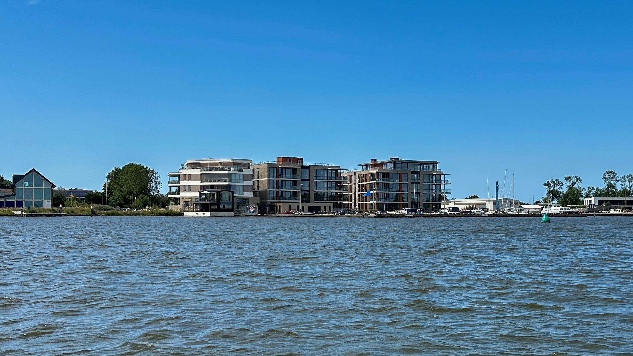 Moderne appartementen en jachthaven aan de waterkant, gezien vanaf het water onder een heldere blauwe lucht