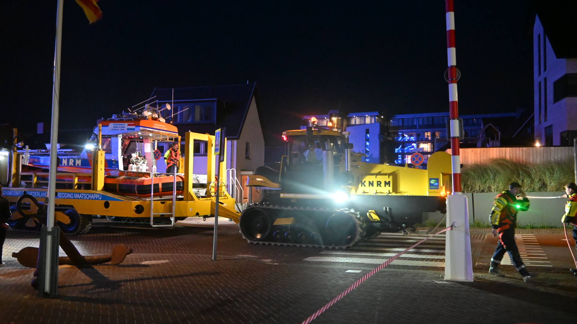 KNRM-reddingsboot op lanceerwagen wordt ’s nachts met werklichten verplaatst, met hulpverleners op de voorgrond