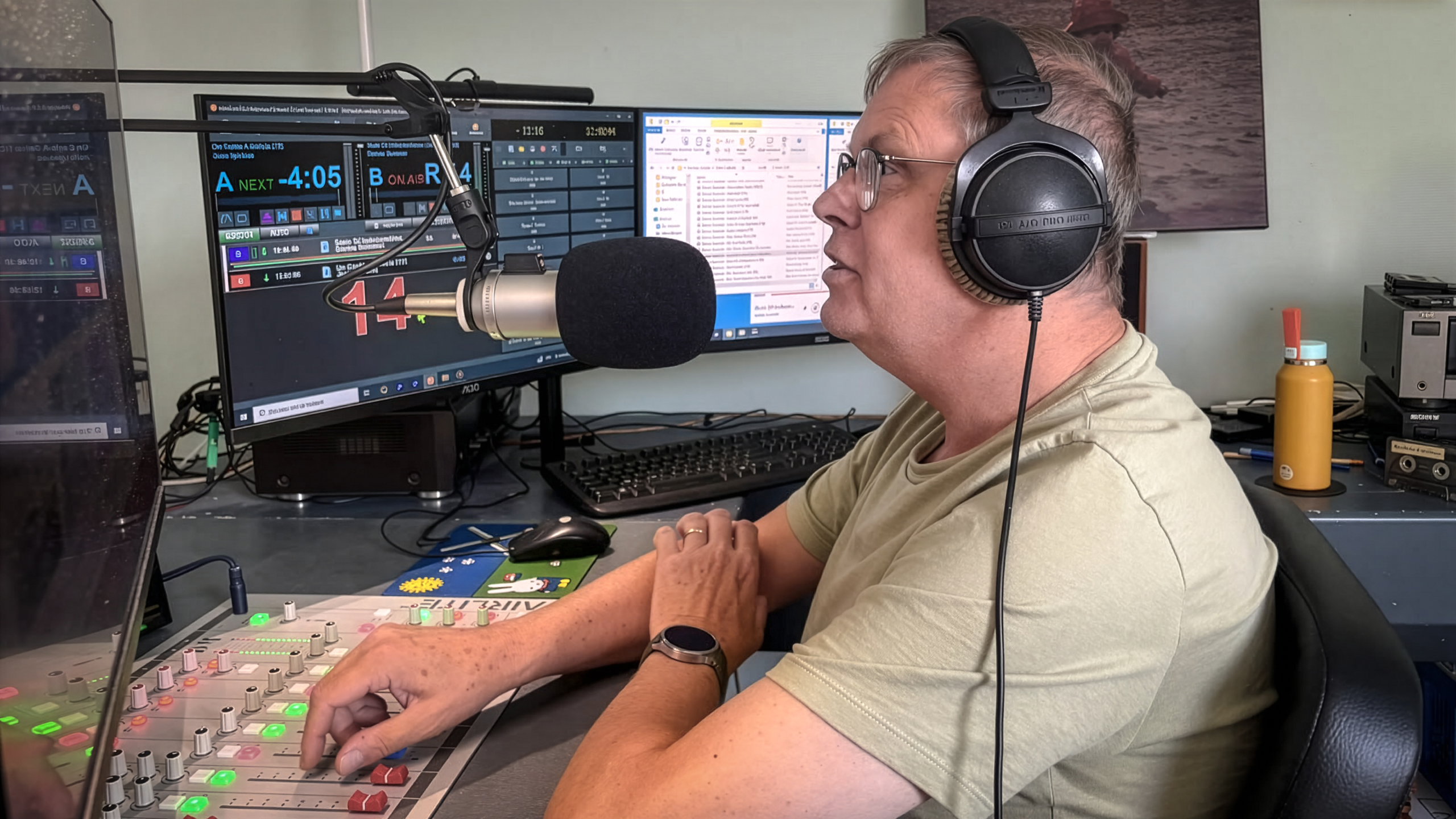 Man met koptelefoon spreekt in studio-microfoon bij mengpaneel en schermen met uitzendingsoftware