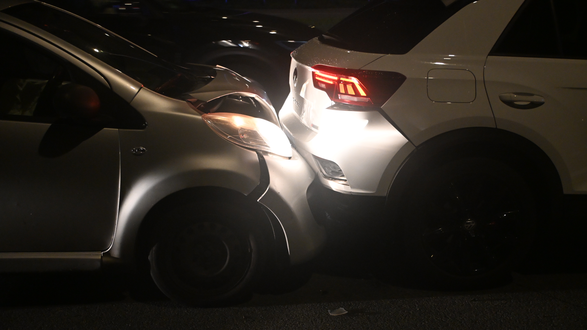 Kop-staartbotsing in het donker, met een grijze auto die achterop een witte auto is gereden