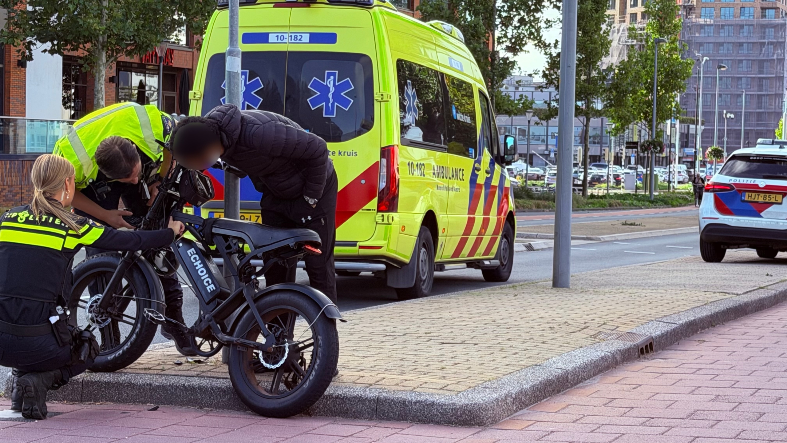 Politie en hulpverleners helpen een persoon bij een e-bike naast een ambulance op straat