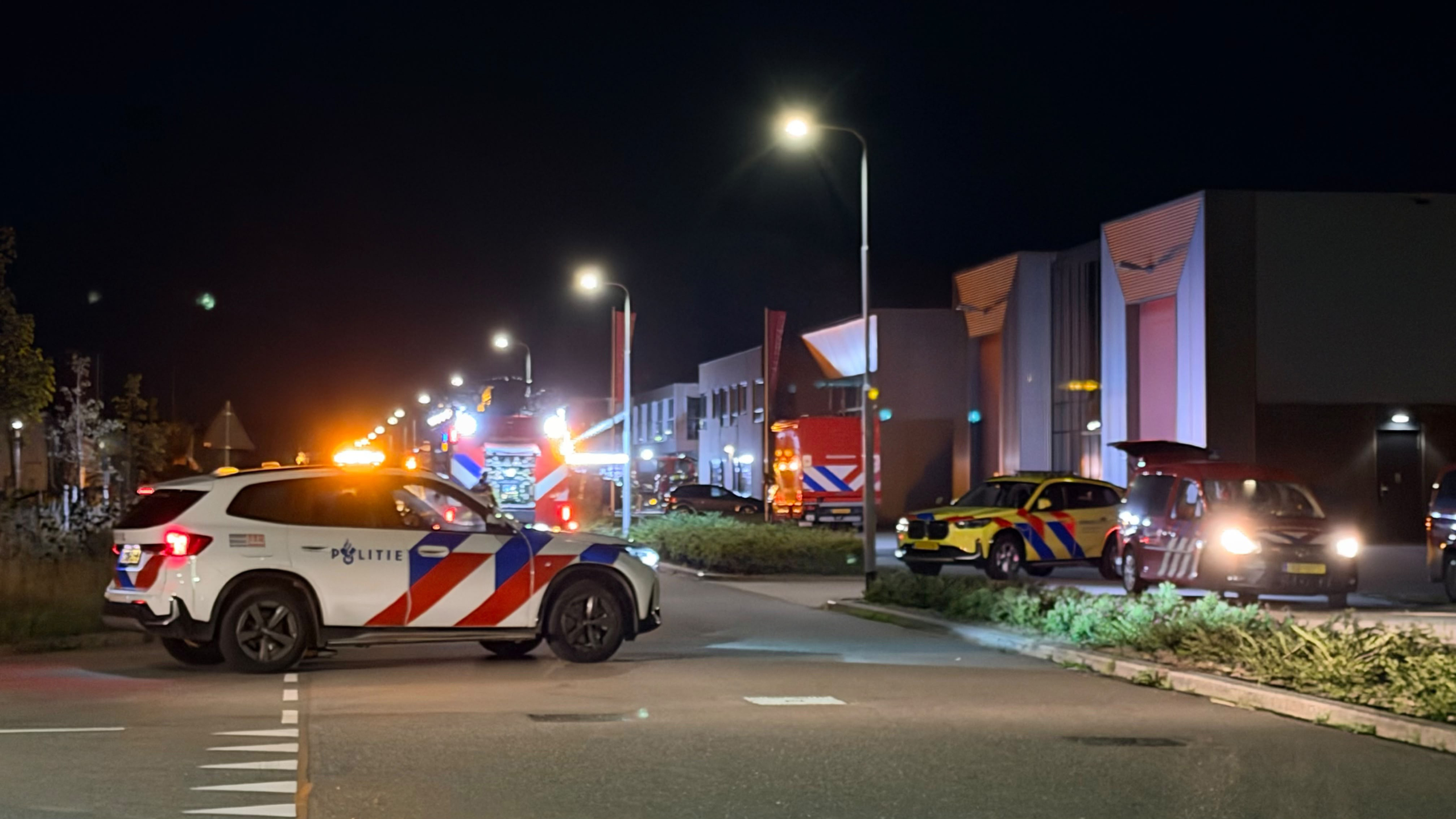 Politieauto en brandweerwagens met zwaailichten op een straat bij bedrijfsgebouwen in de nacht