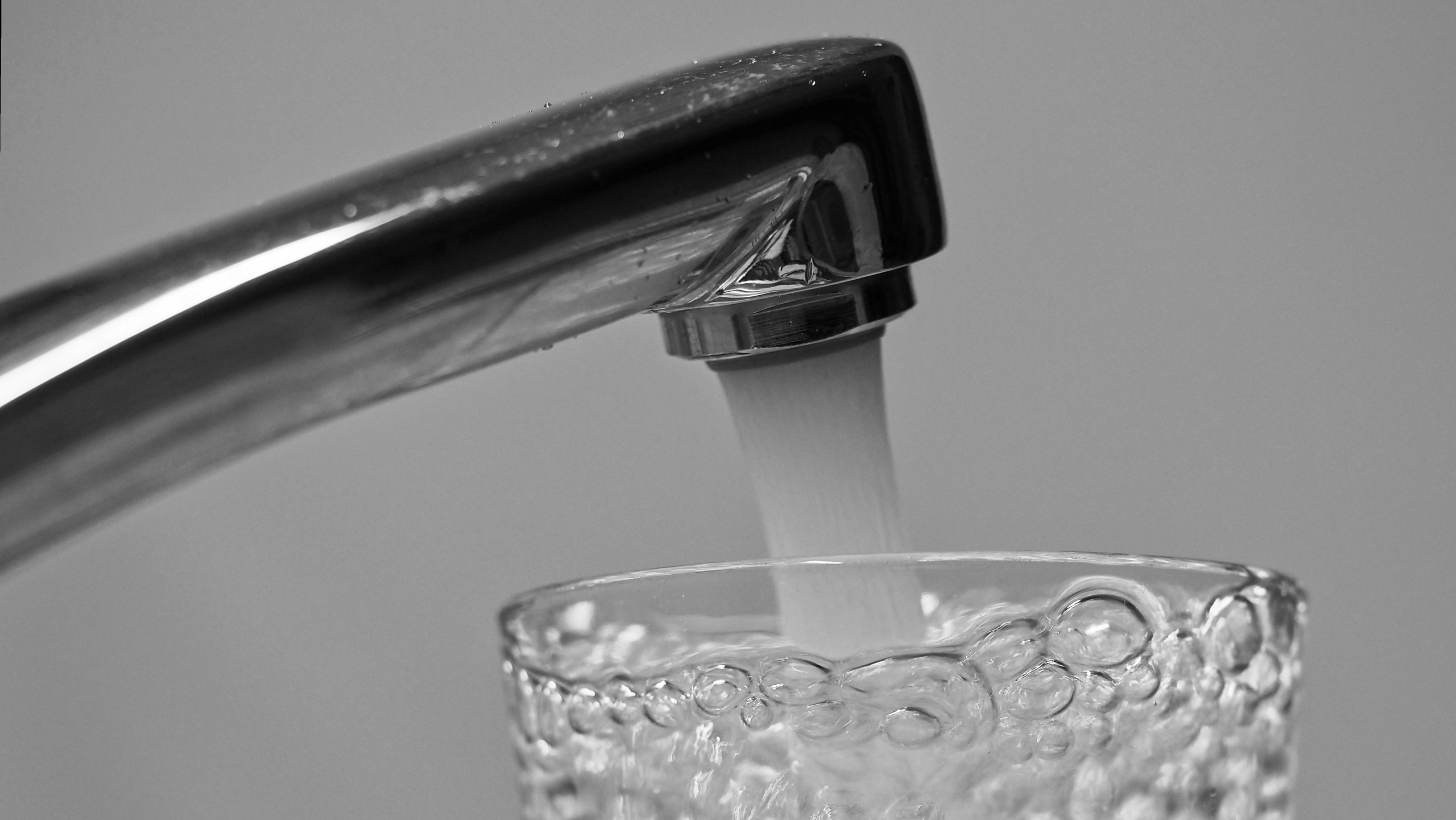 Close-up van een kraan waar water in een glas stroomt, met zichtbare bubbels in het water
