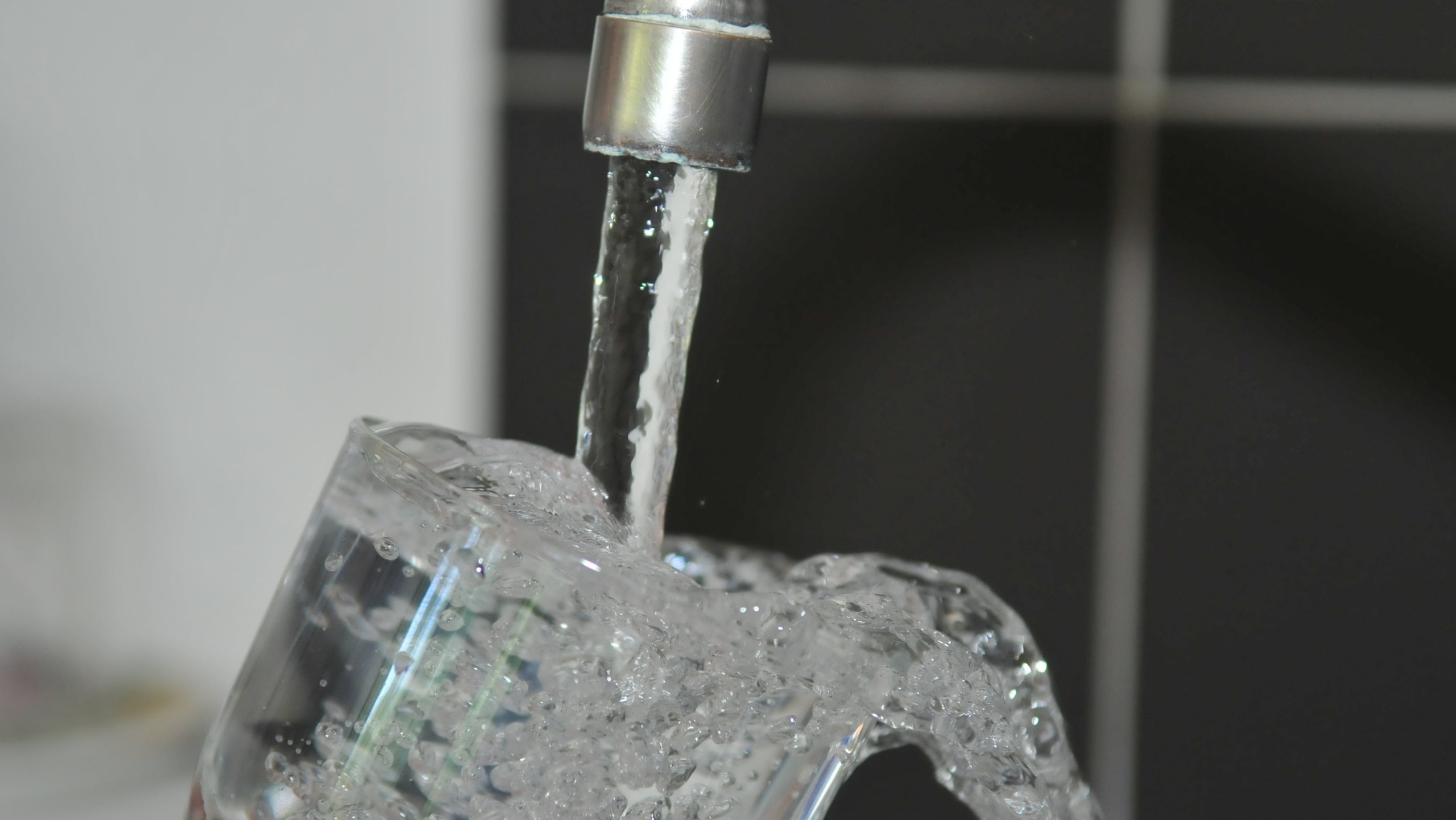 Water stroomt uit een kraan in een scheef gehouden glas, waardoor het glas overloopt en spat