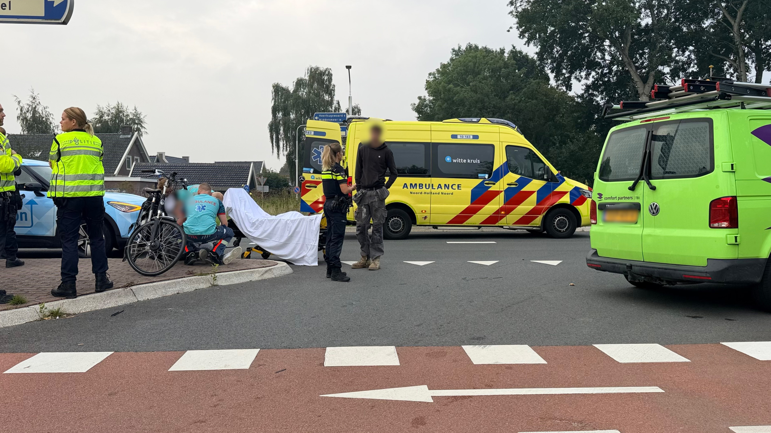 Hulpdiensten bij verkeersincident: politie, ambulance en brancard met afscherming naast een fiets op kruispunt