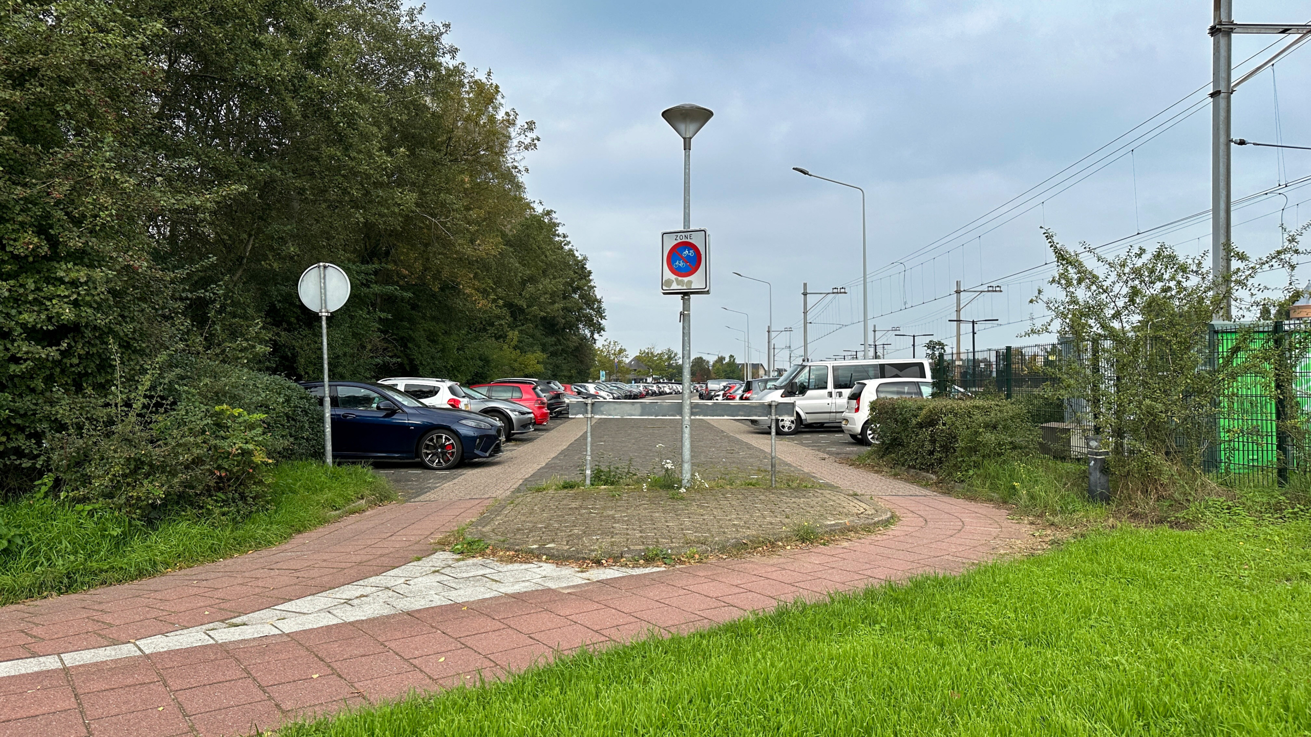 Ingang naar parkeerterrein met slagboom, geparkeerde auto’s en bord “zone” met fiets- en bromfietsverbod