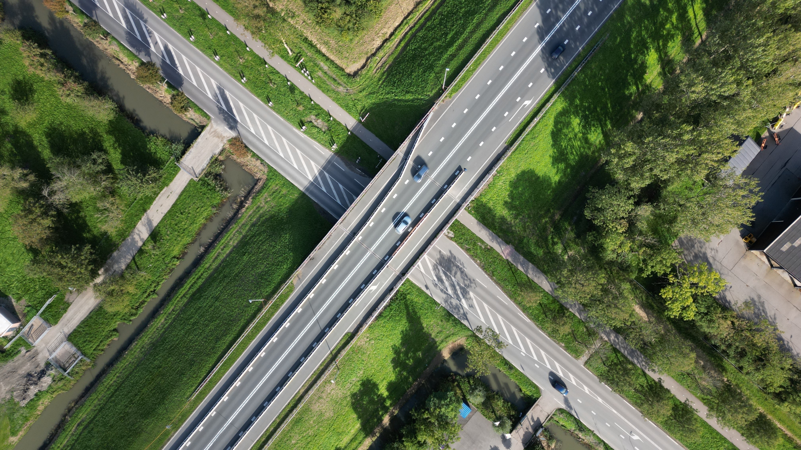 Luchtfoto van een kruispunt met een viaduct waar auto’s rijden, omringd door groen en een smal kanaal