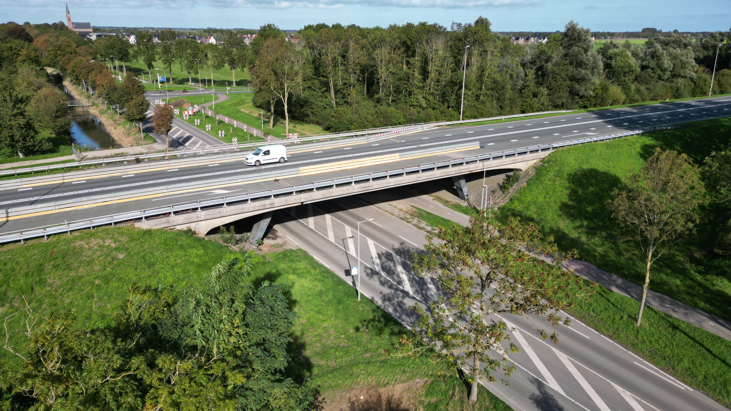 Luchtfoto van een viaduct met een witte bestelwagen, boven een kruising met wegen en groen landschap