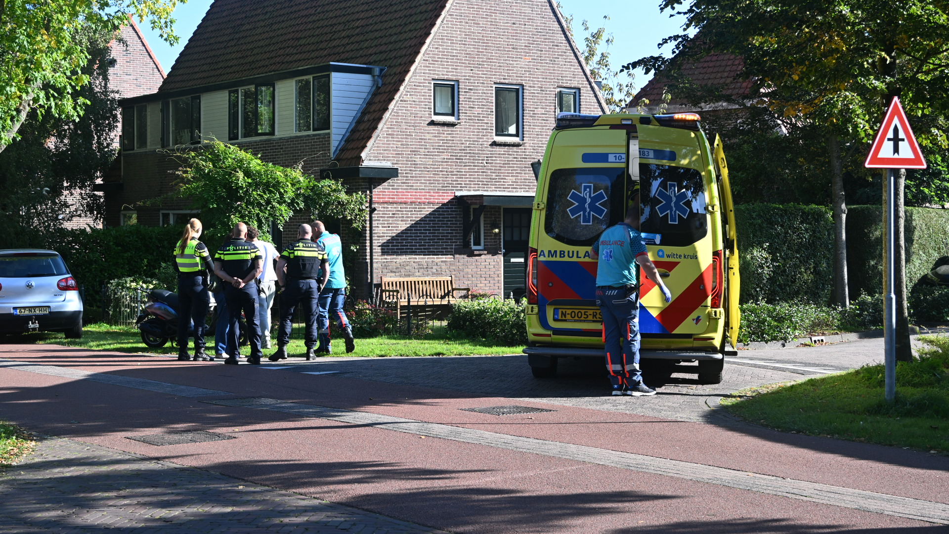 Ambulance met open achterdeur en politieagenten bij een woning in een rustige woonwijk