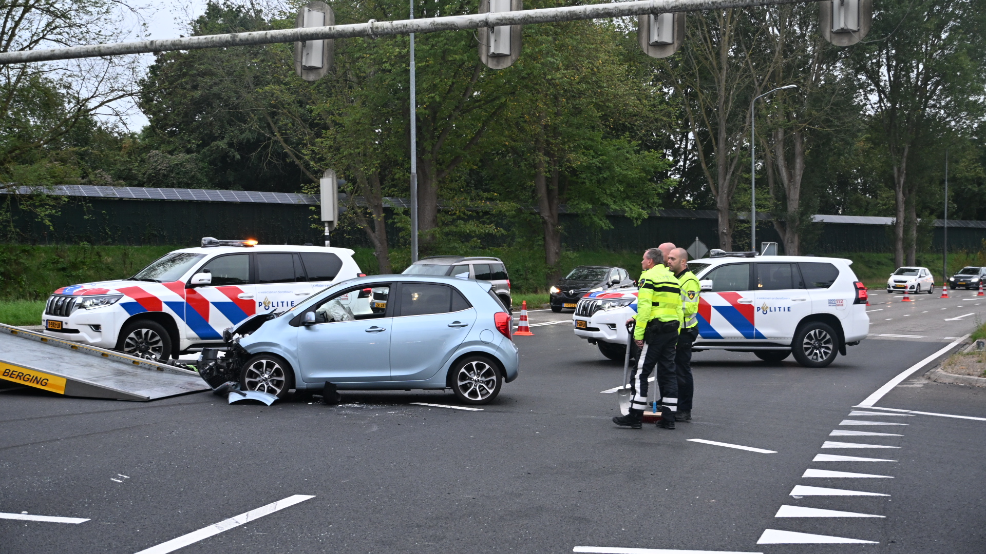 Beschadigde lichtblauwe auto wordt weggesleept na ongeval, met Nederlandse politieauto’s en agenten op kruispunt