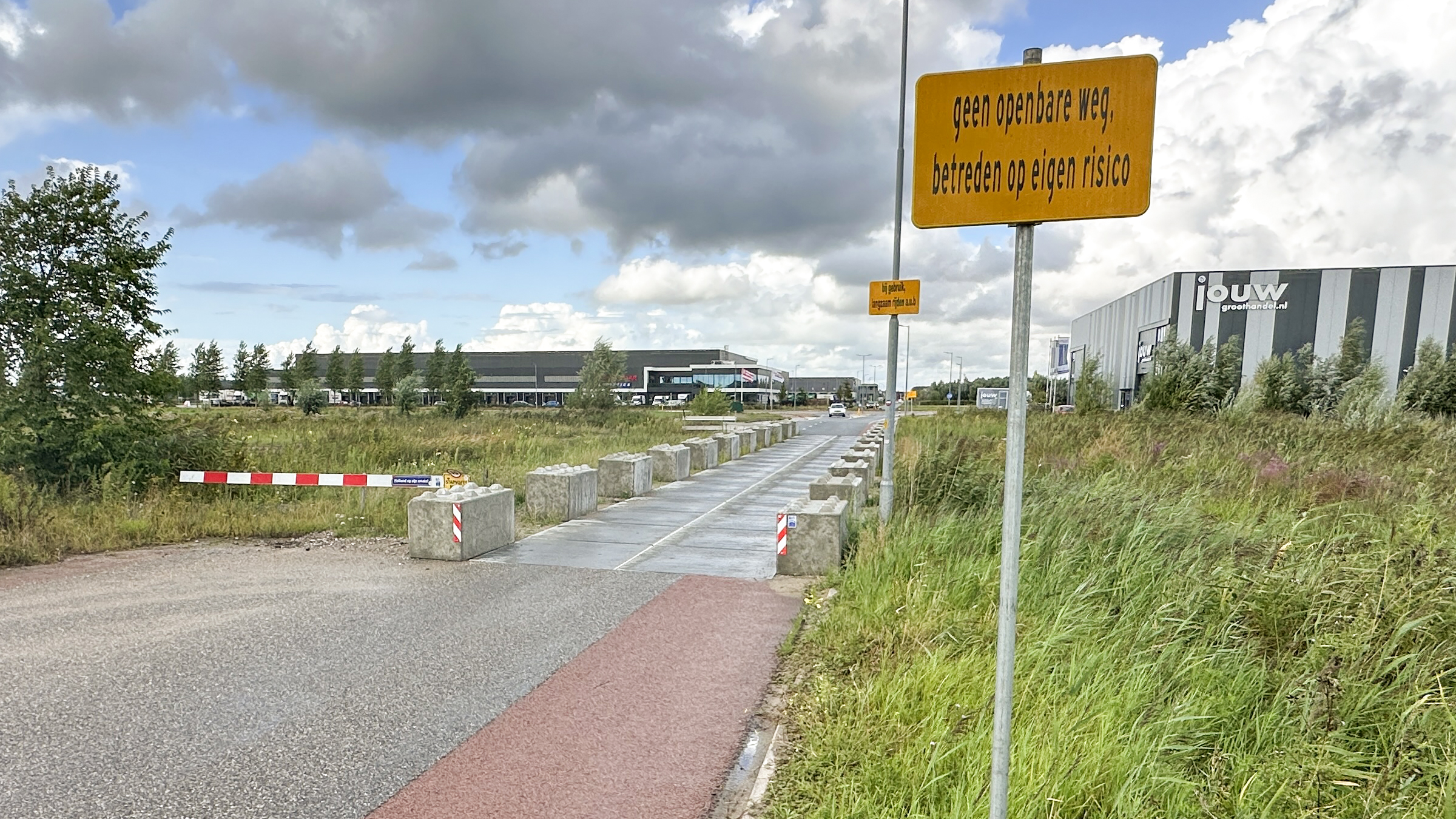 Gele waarschuwingsborden “geen openbare weg, betreden op eigen risico” bij toegangsweg met betonblokken