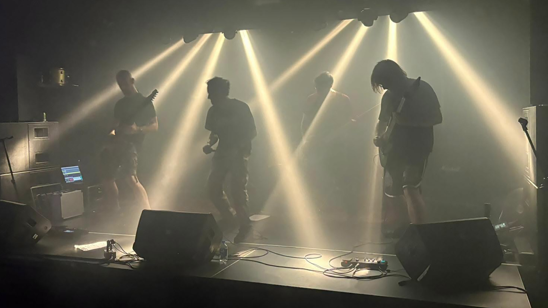 Band treedt op op een rokerig podium, silhouetten met gitaren en microfoon in felle lichtbundels