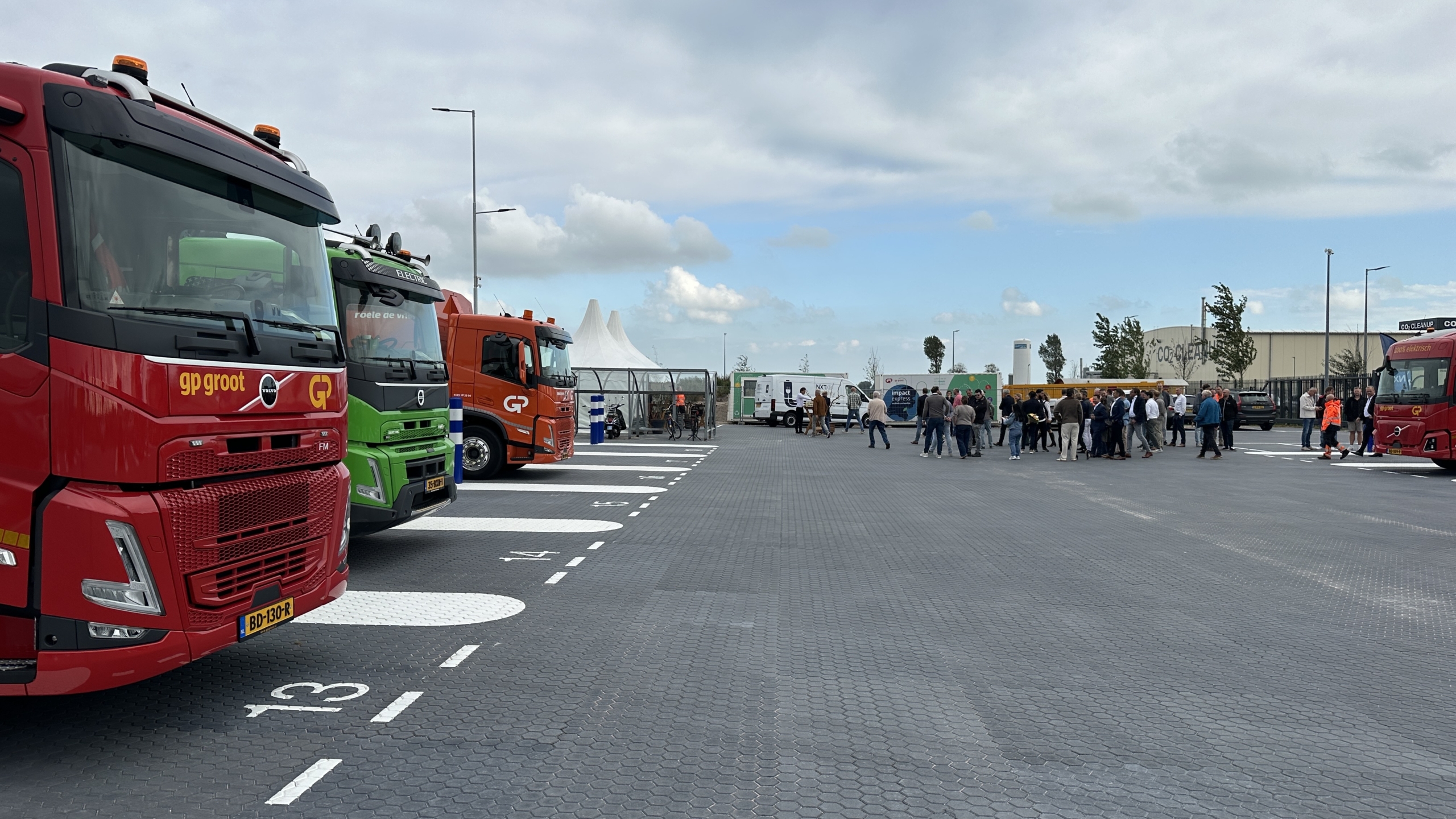 Geparkeerde rode, groene en oranje vrachtwagens op een terrein, met een groep mensen die samenstaat op de achtergrond