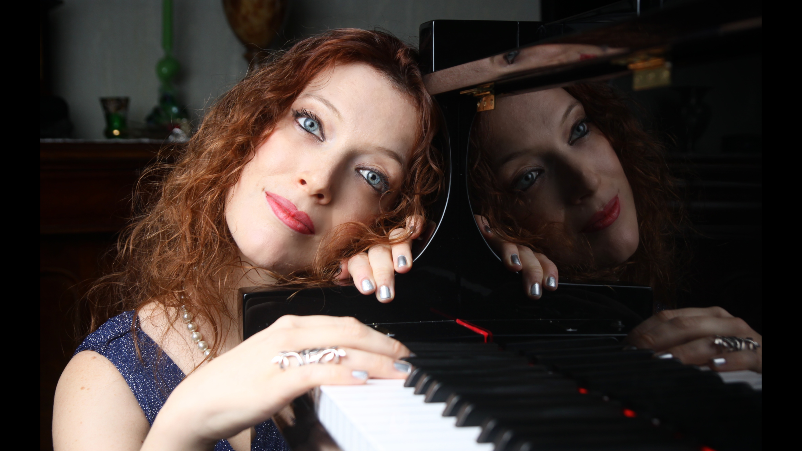 Portret van vrouw met rood krullend haar die met haar hoofd op een piano leunt, met spiegeling in de glanzende piano
