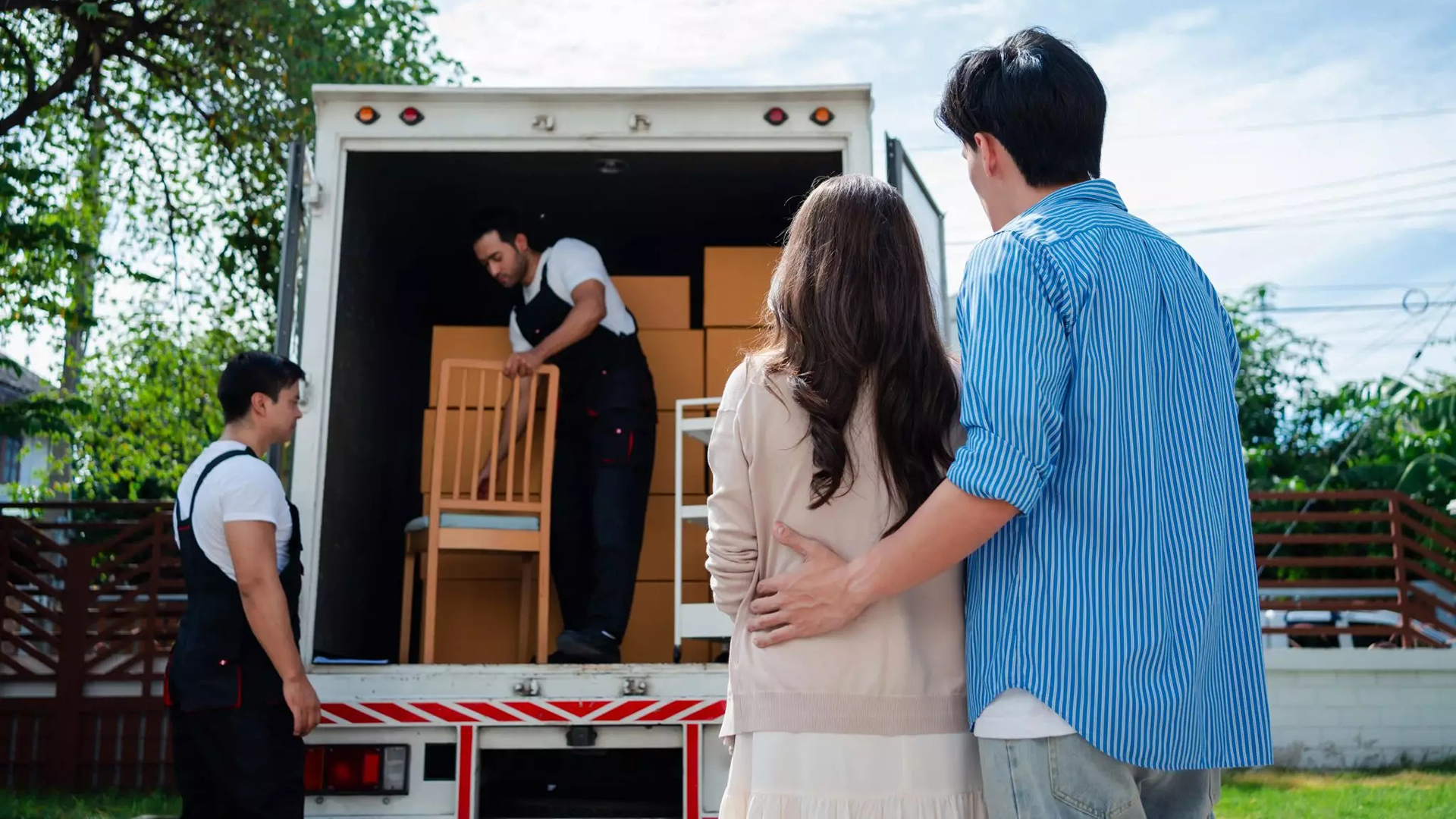 Stel kijkt naar verhuizers die dozen en een stoel in een verhuiswagen laden bij een huis