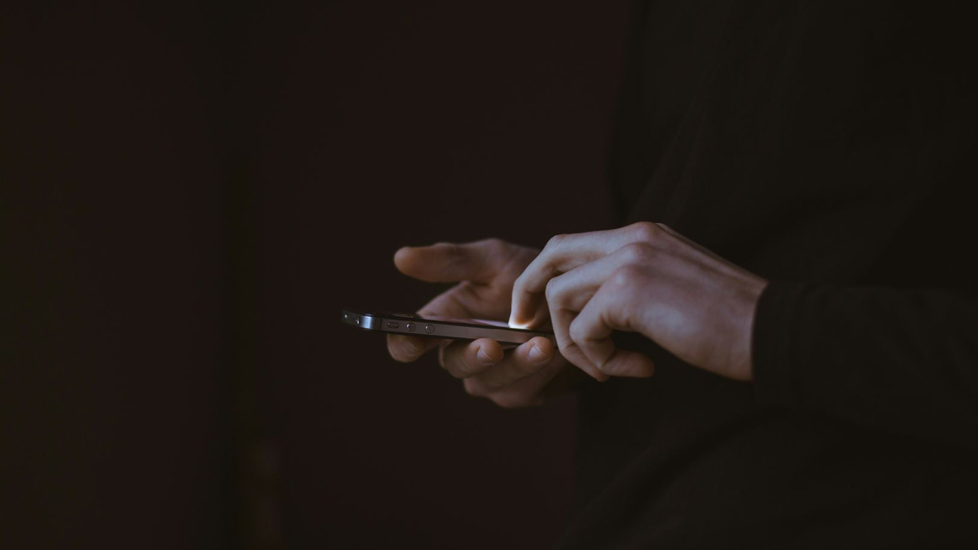 Close-up van handen die in het donker op een smartphone tikken