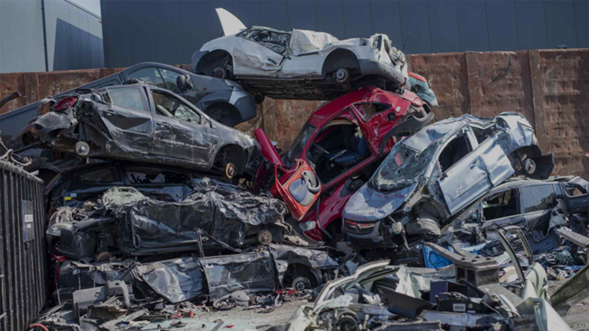 Stapel zwaar beschadigde auto’s op een autokerkhof, met wrakken op elkaar en losse onderdelen op de grond