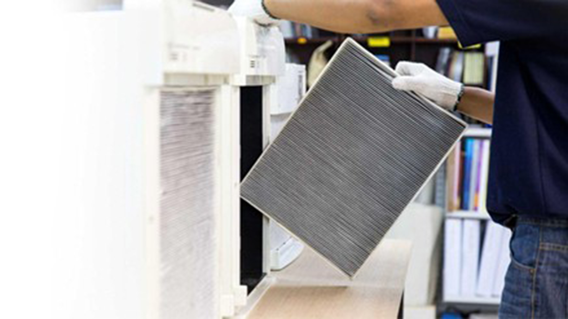 Persoon met handschoen verwijdert een luchtfilter uit een ventilatie- of airco-unit op een werkbank