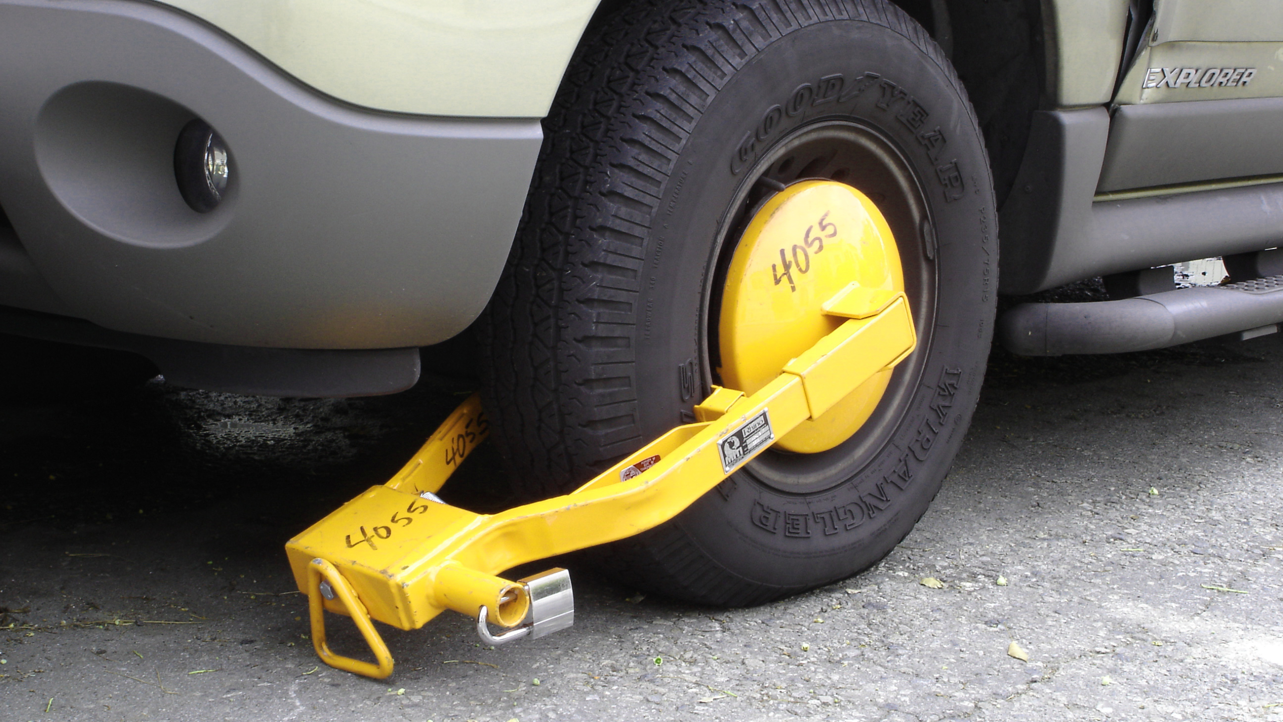 Autowiel van SUV met gele wielklem en hangslot op een parkeerplaats