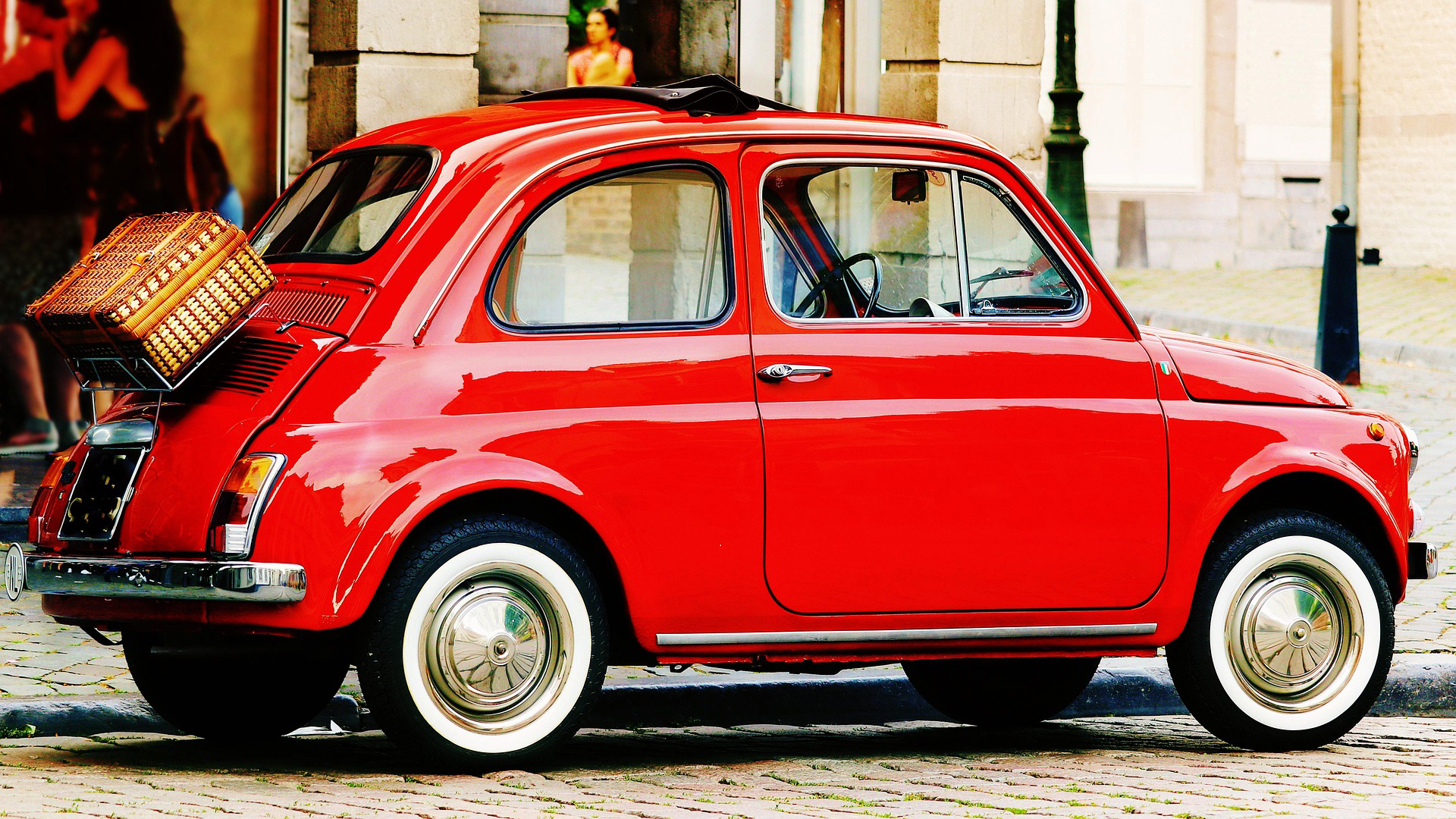 Rode klassieke Fiat 500 geparkeerd op kasseien, met rieten koffer op de achterdrager