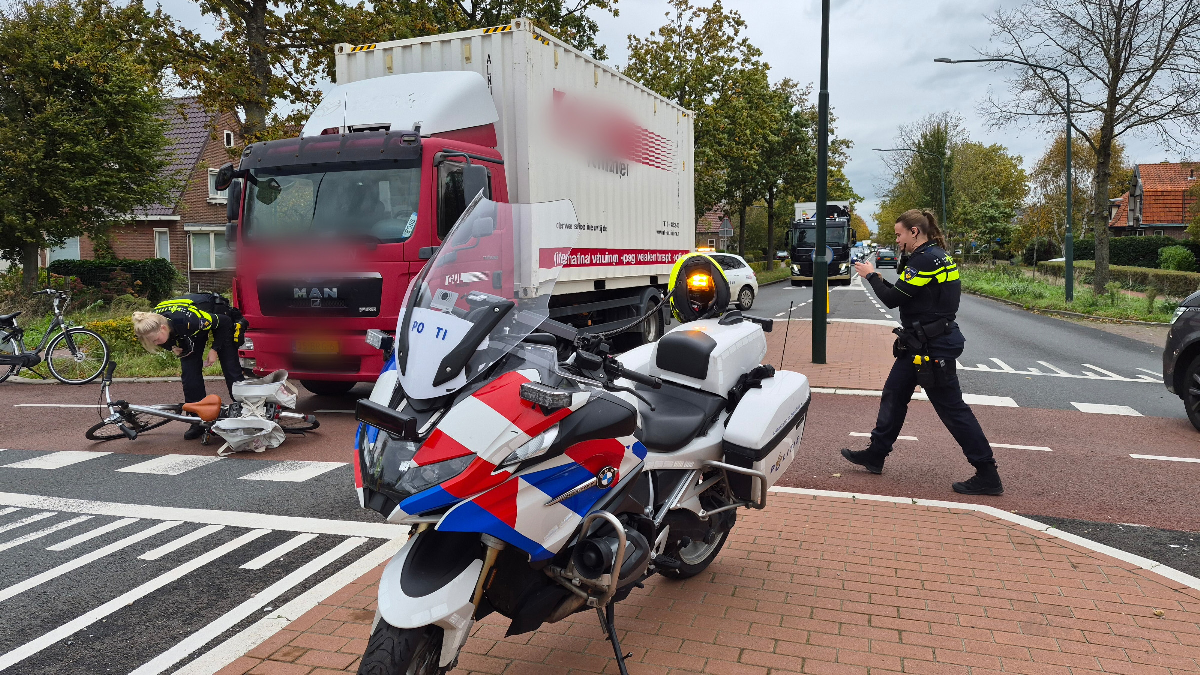 Politieagenten bij een verkeersincident met een gevallen fiets naast een rode vrachtwagen en een politiemotor op de voorgrond