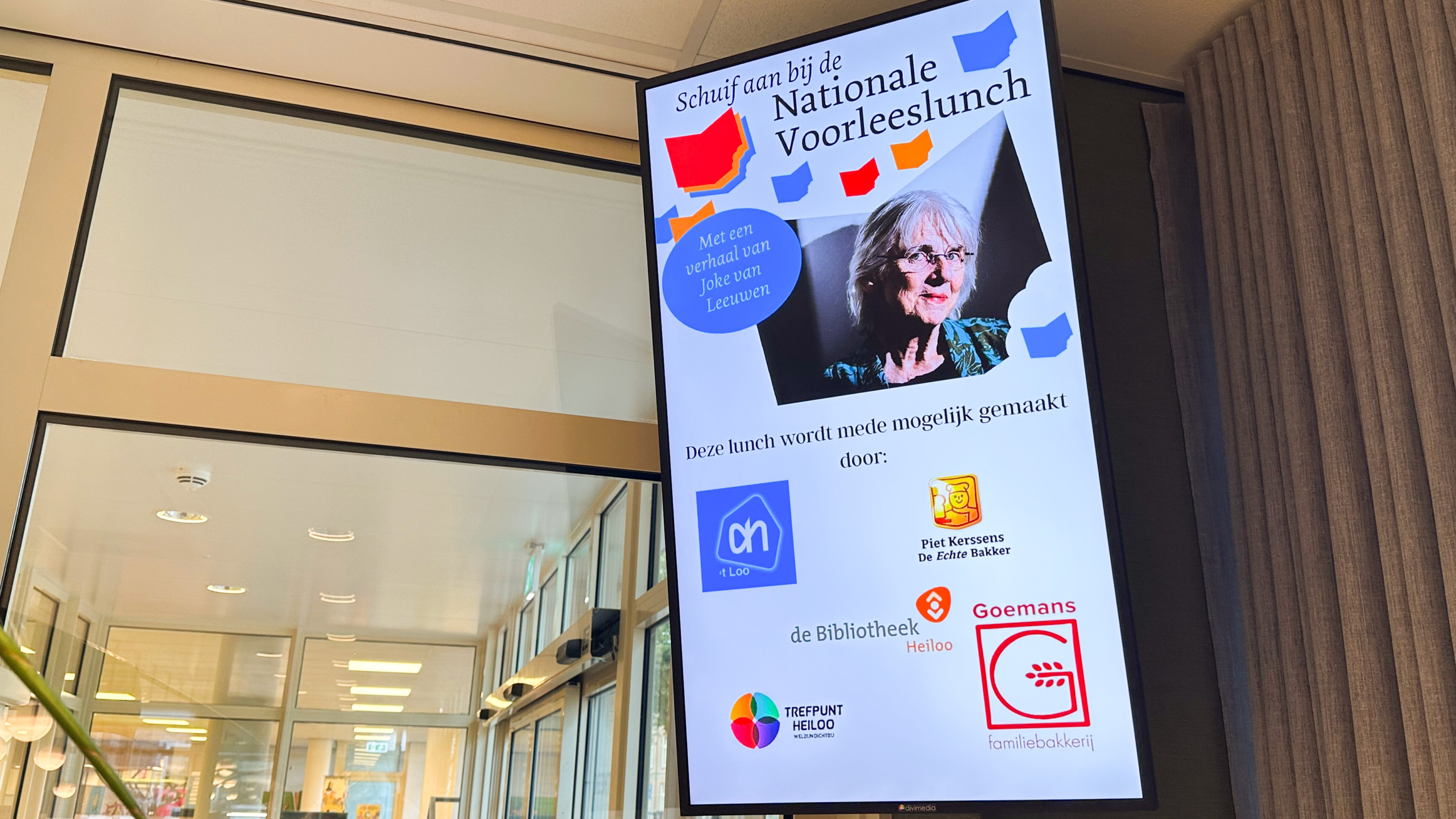Digitaal scherm met poster voor de Nationale Voorleeslunch, met portret van Joke van Leeuwen en sponsors