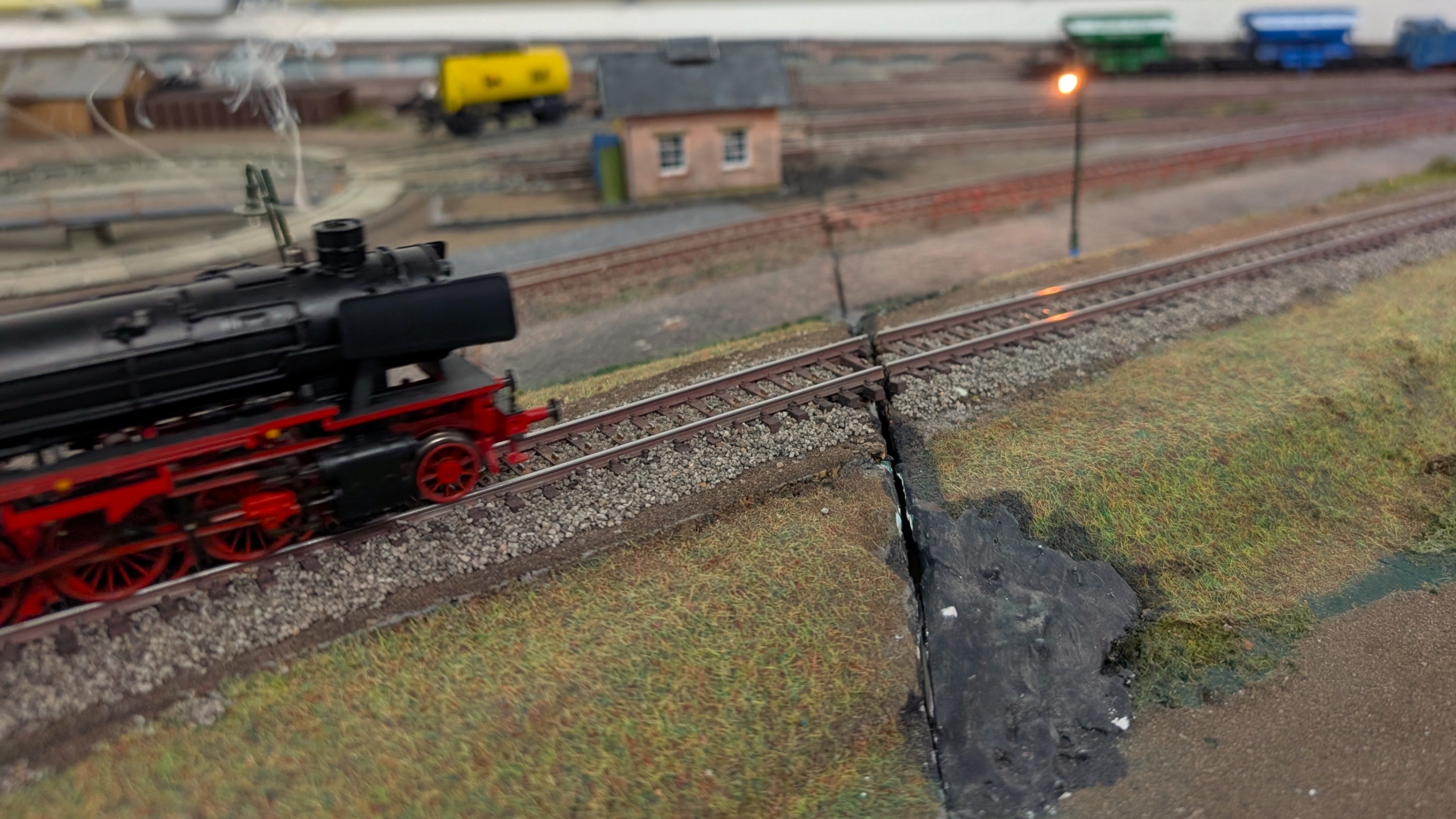 Modelspoorbaan met zwarte stoomlocomotief op rails, achtergrond met seinhuisje en brandende lantaarn