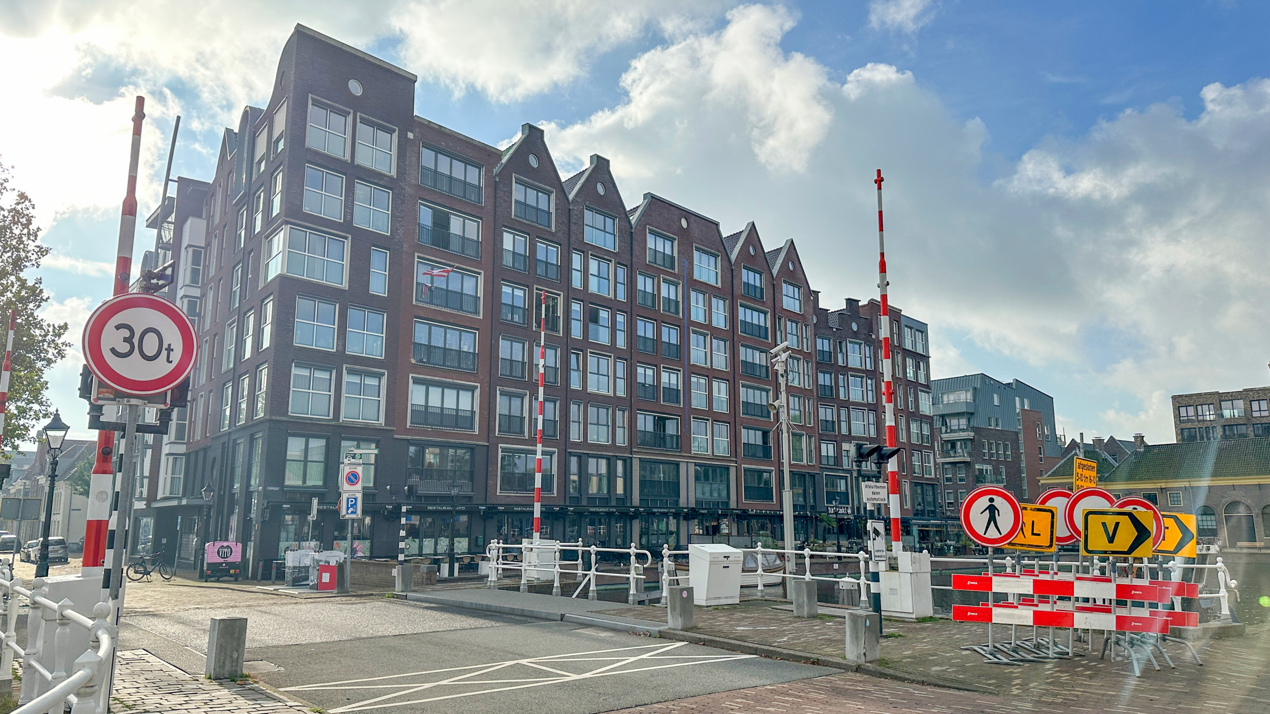 Groot modern bakstenen appartementencomplex aan een brug, met rood-witte slagbomen en verkeersborden (30t)