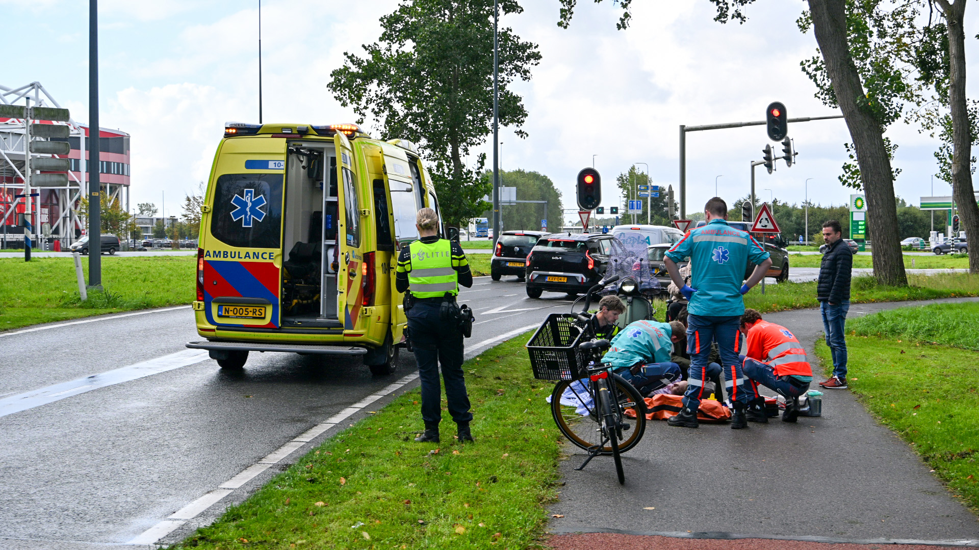 Ambulance en politie bij kruispunt; hulpverleners behandelen persoon op fietspad naast een omgevallen fiets