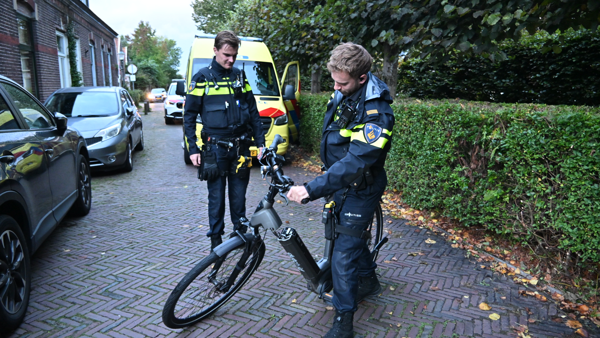 Twee politieagenten inspecteren een e-bike op een straat, met een politieauto op de achtergrond