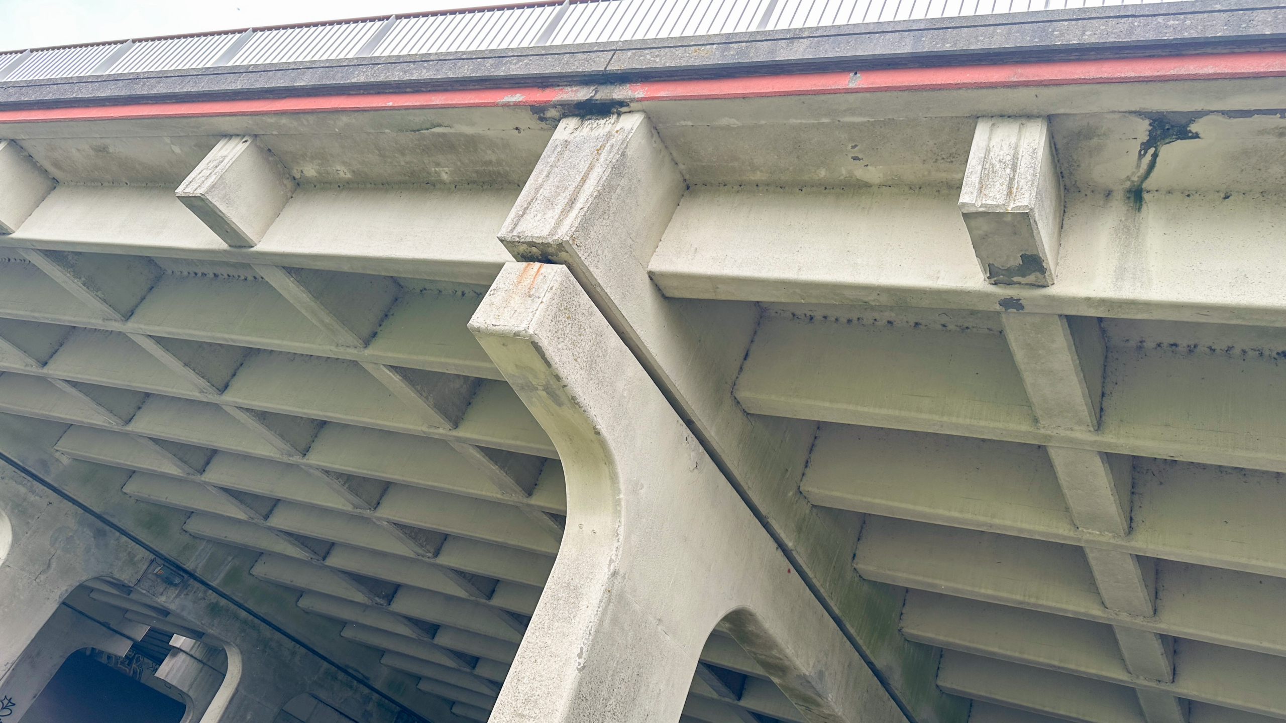 Onderzijde van een betonnen brug met ribbenstructuur en draagbalken, met donkere vocht- en roestvlekken langs de rand