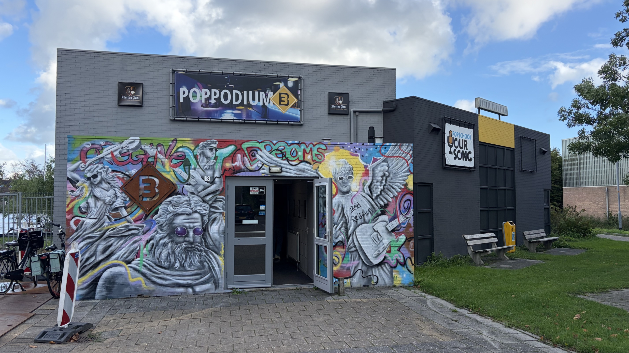 Gevel van poppodium B met kleurrijke graffiti en bord “POPPODIUM B”, open ingang en fietsen links