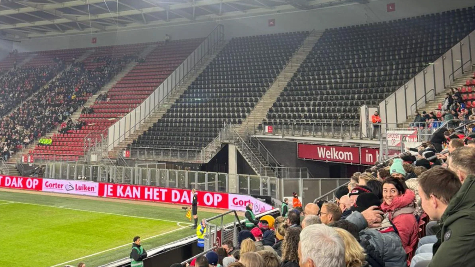 Tribune van een voetbalstadion met toeschouwers langs de zijlijn en het bord met tekst Welkom in k